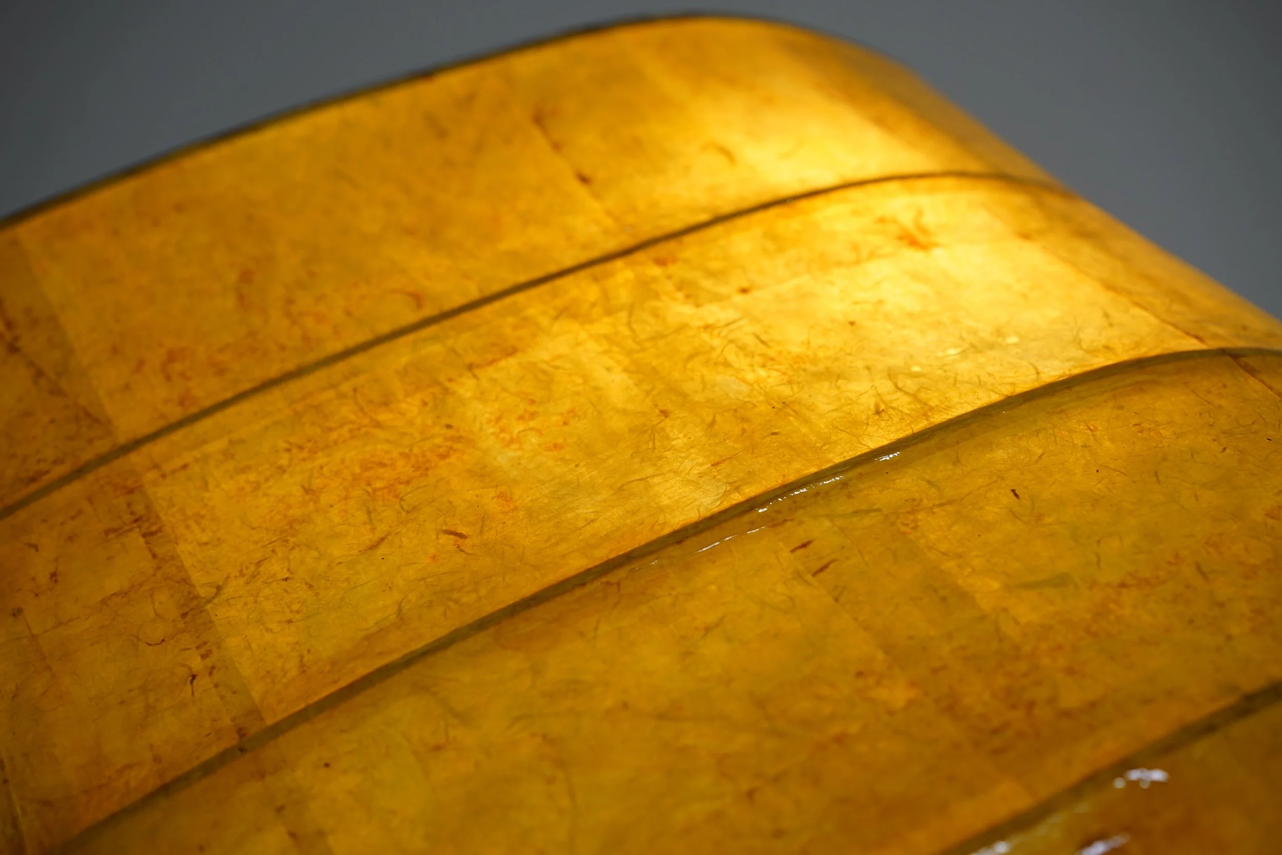 Close-up of yellowish-brown textured paper or fabric, folded with visible fibers and lines.