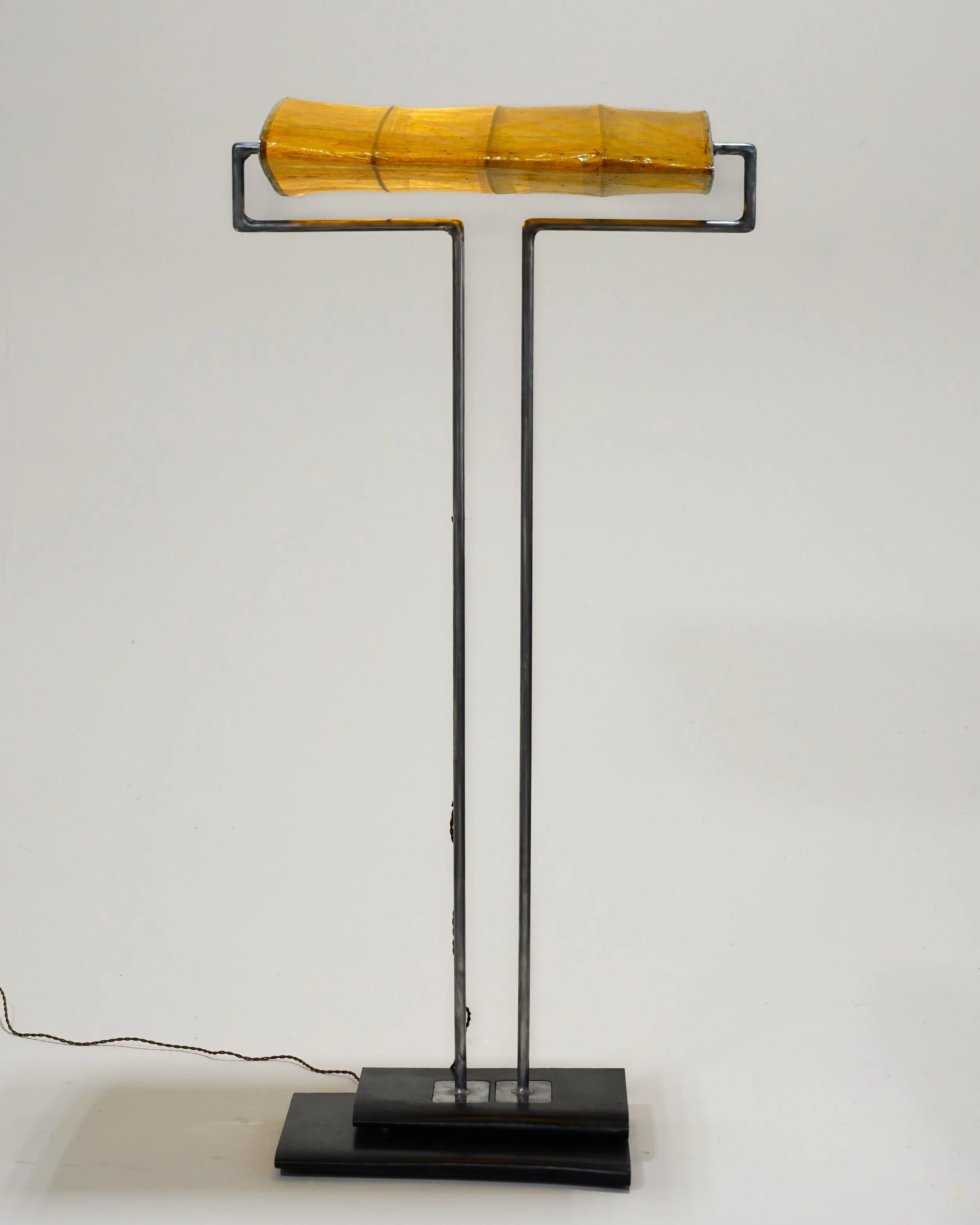 A walking cane with a light brown bamboo handle and a black metal shaft, mounted on a black base.