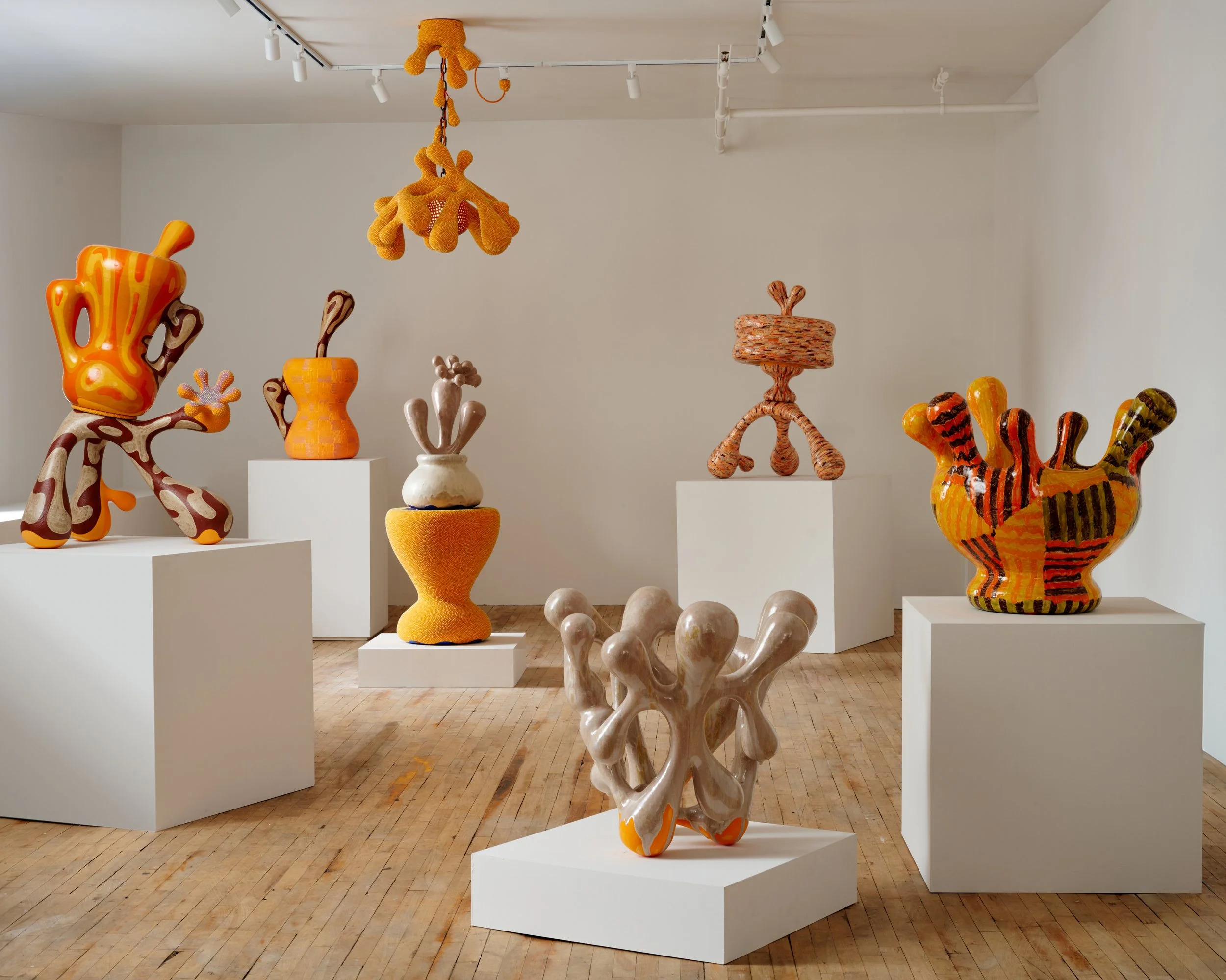 Art sculptures in an art gallery, featuring abstract and colorful forms on white pedestals. Joël Brodovsky-Adams.