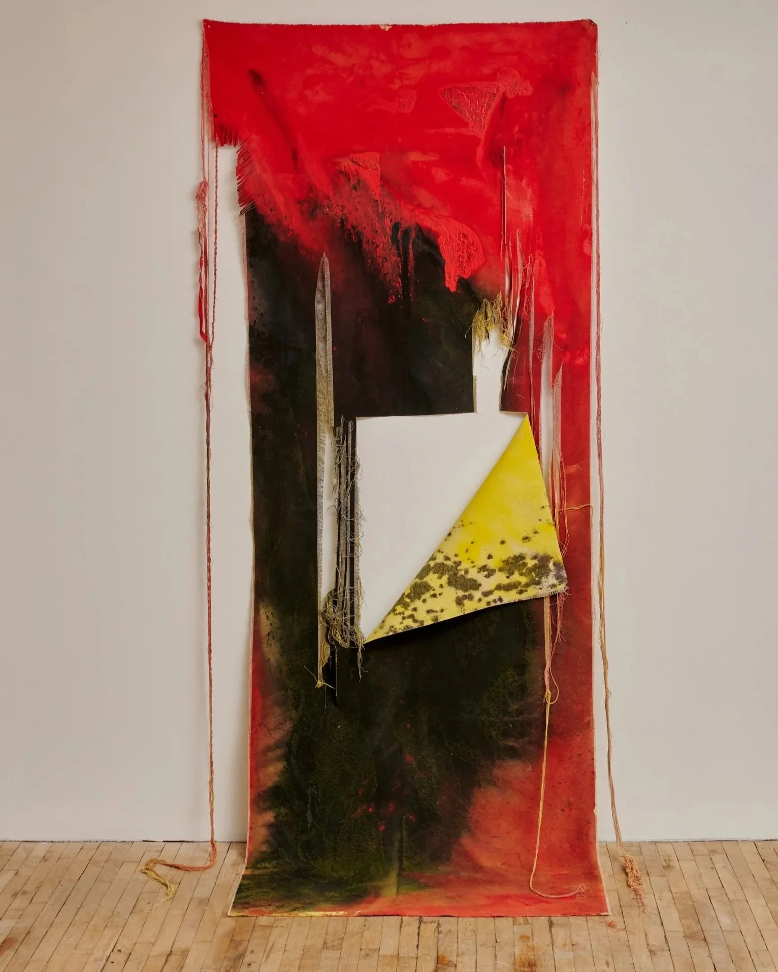 An art piece featuring a large, abstract letter 'F' with a red, black, and dark blue color palette, made of mixed media materials that include fabric and paint, displayed against a white wall. Vaughn Davis Jr.