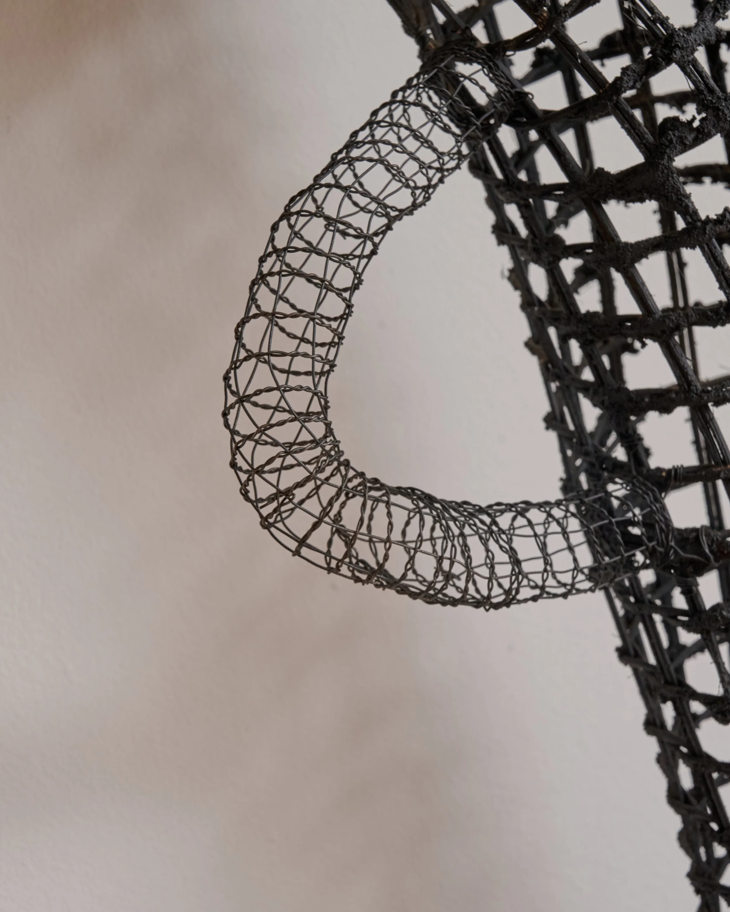 Close-up of a black wire sculpture with a curved handle or arm, against a plain light background.