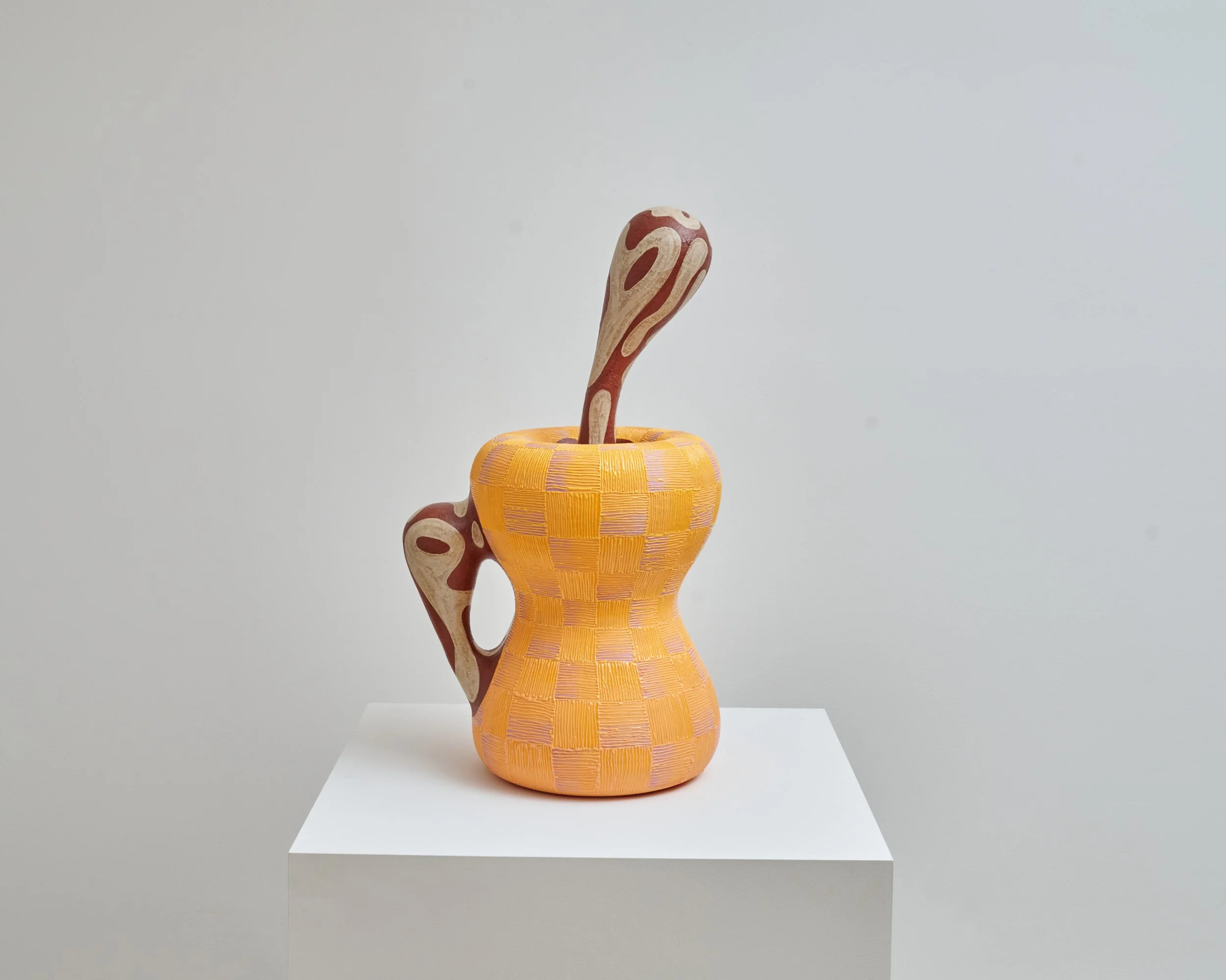 Ceramic sculpture of a snake coiled inside a wide, orange basket with yellow accents, on a white pedestal against a plain background. Joël Brodovsky-Adams.