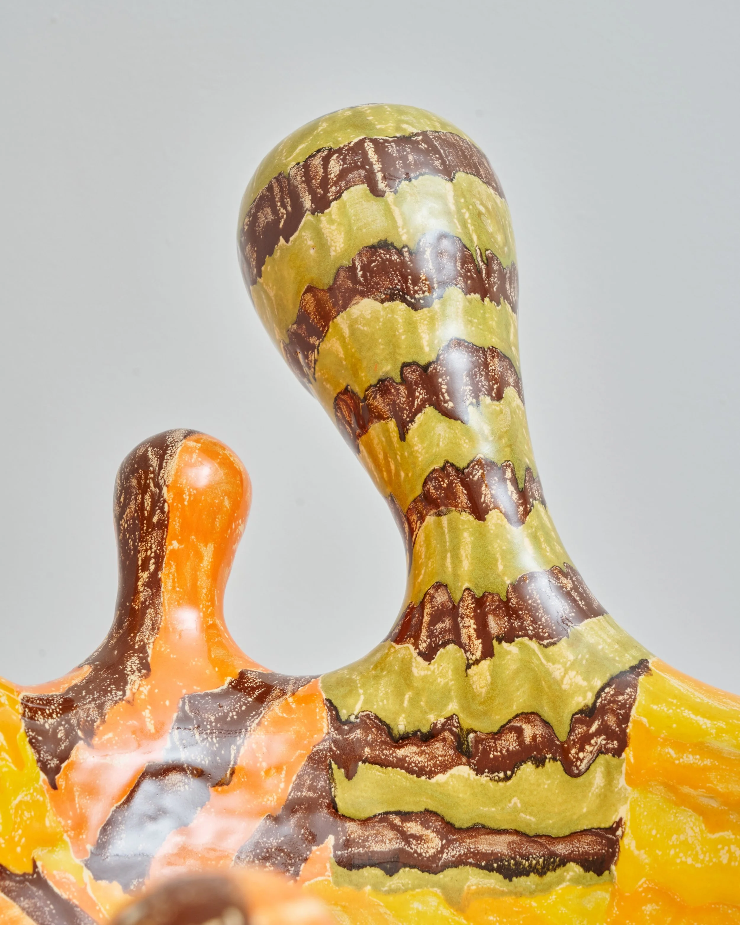 Close-up of a multicolored decorative object with a striped pattern in yellow, brown, orange, and gray, against a plain light background. Joël Brodovsky-Adams.