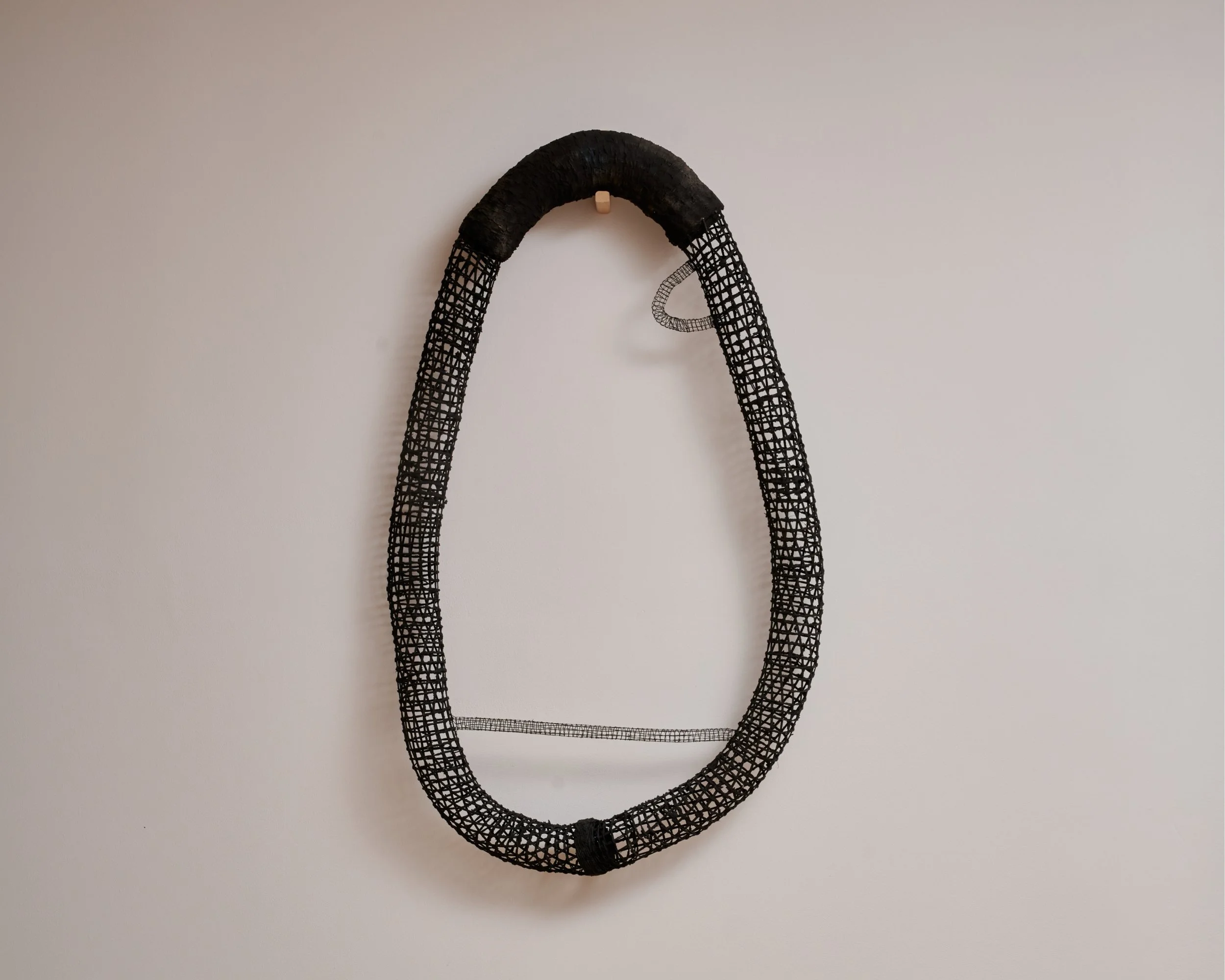 A black fishing net with a mesh pattern hangs on a plain white wall.
