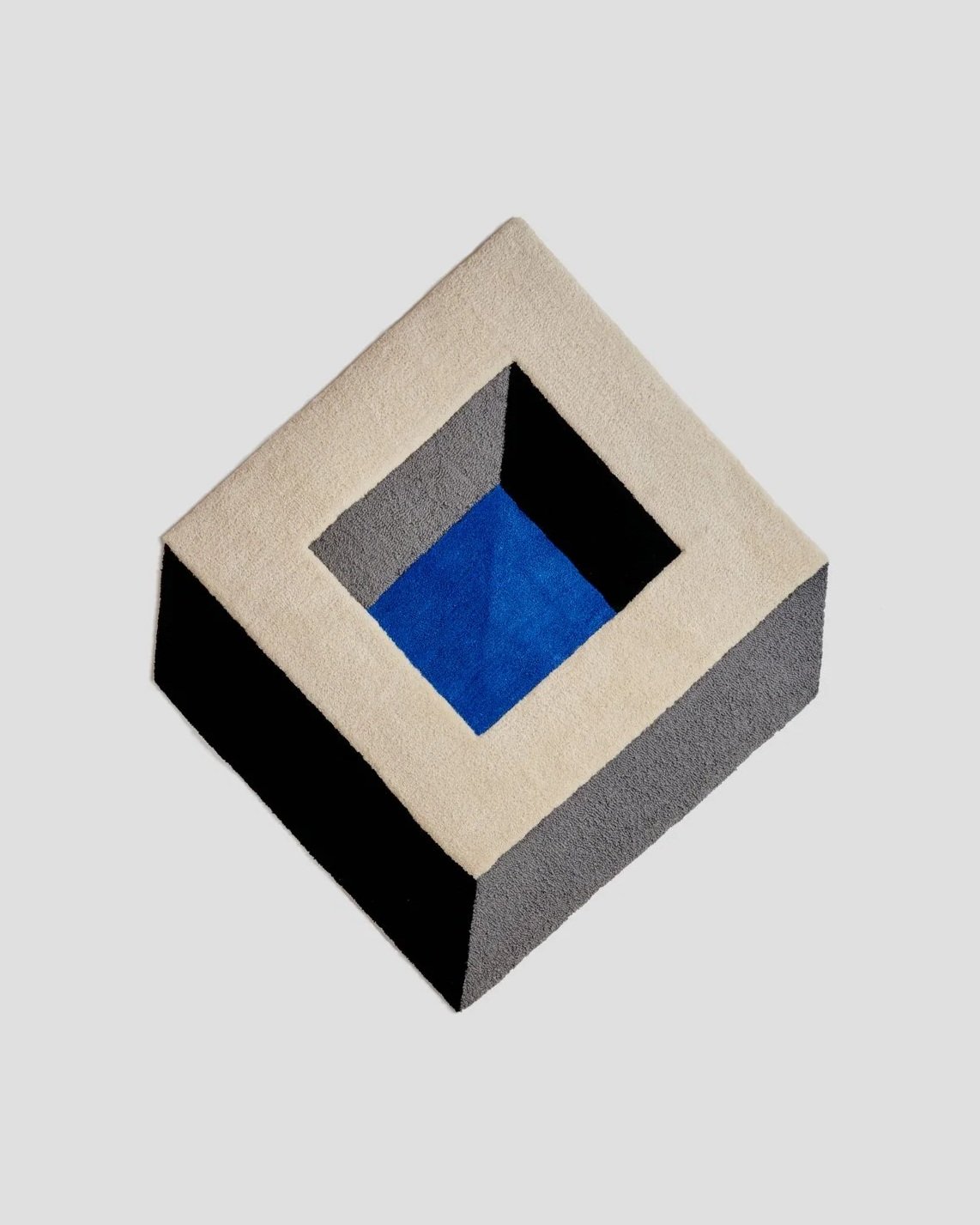 A geometric abstract rug with a layered square and triangular pattern in shades of black, gray, blue, and cream.