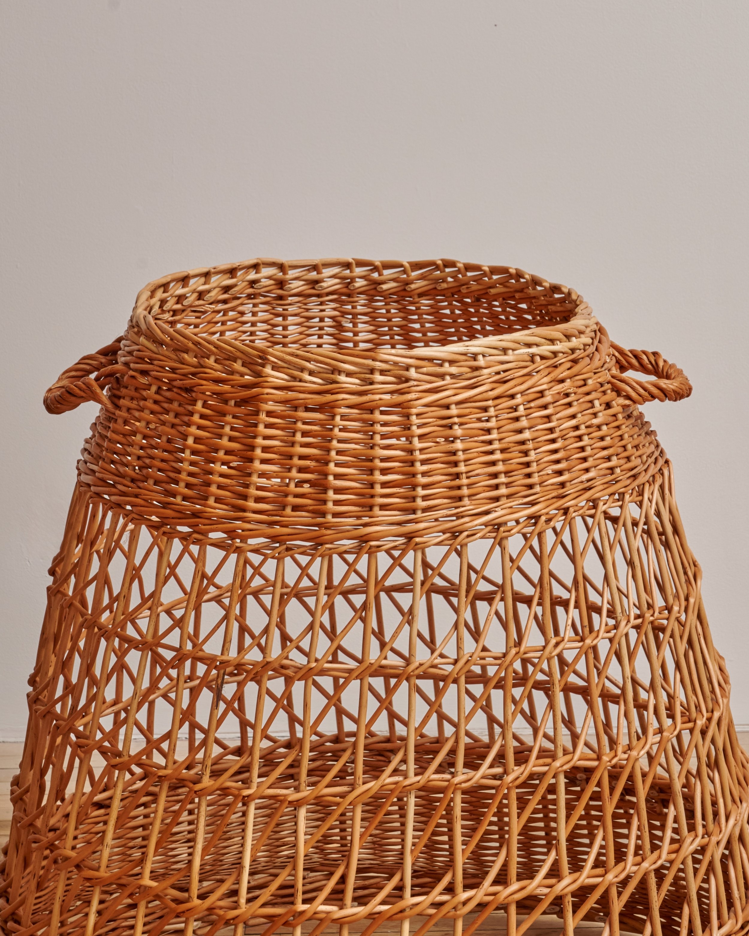 Three-tiered woven wicker basket stand against a plain wall.