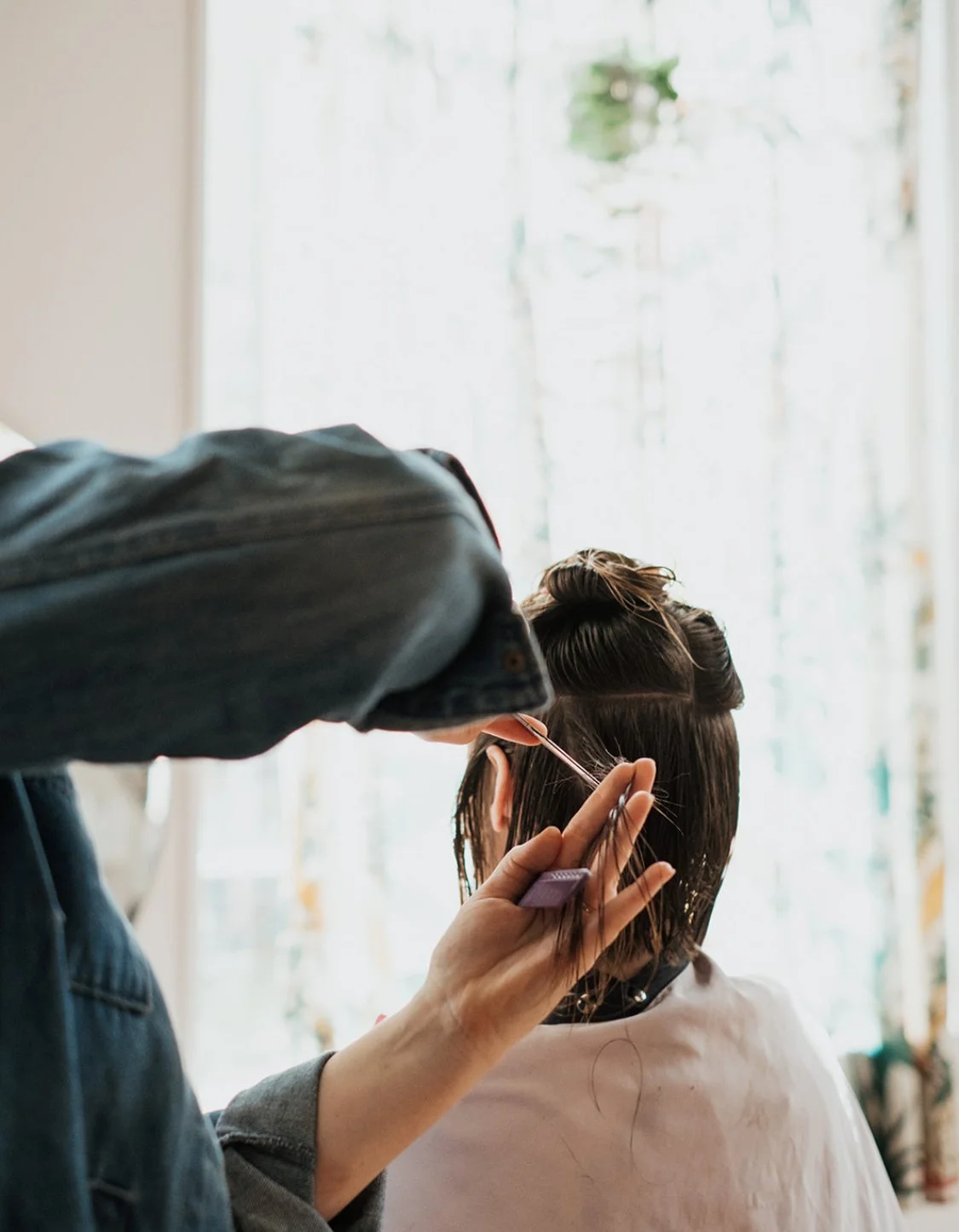 A hairstylist a Ceremony Salon in Carrboro NC cutting hair in a bright studio.