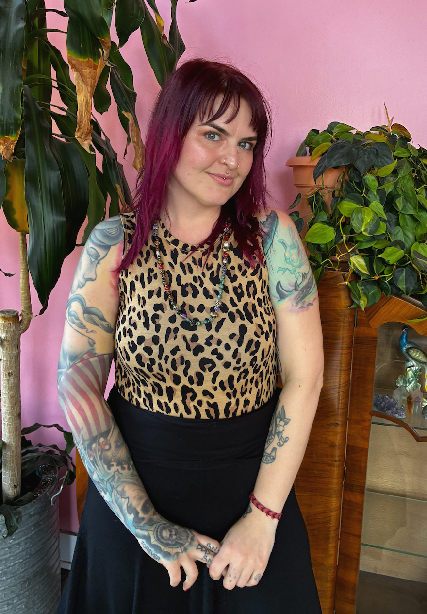 woman standing near a plant in a hair salon wearing a leopard print shirt