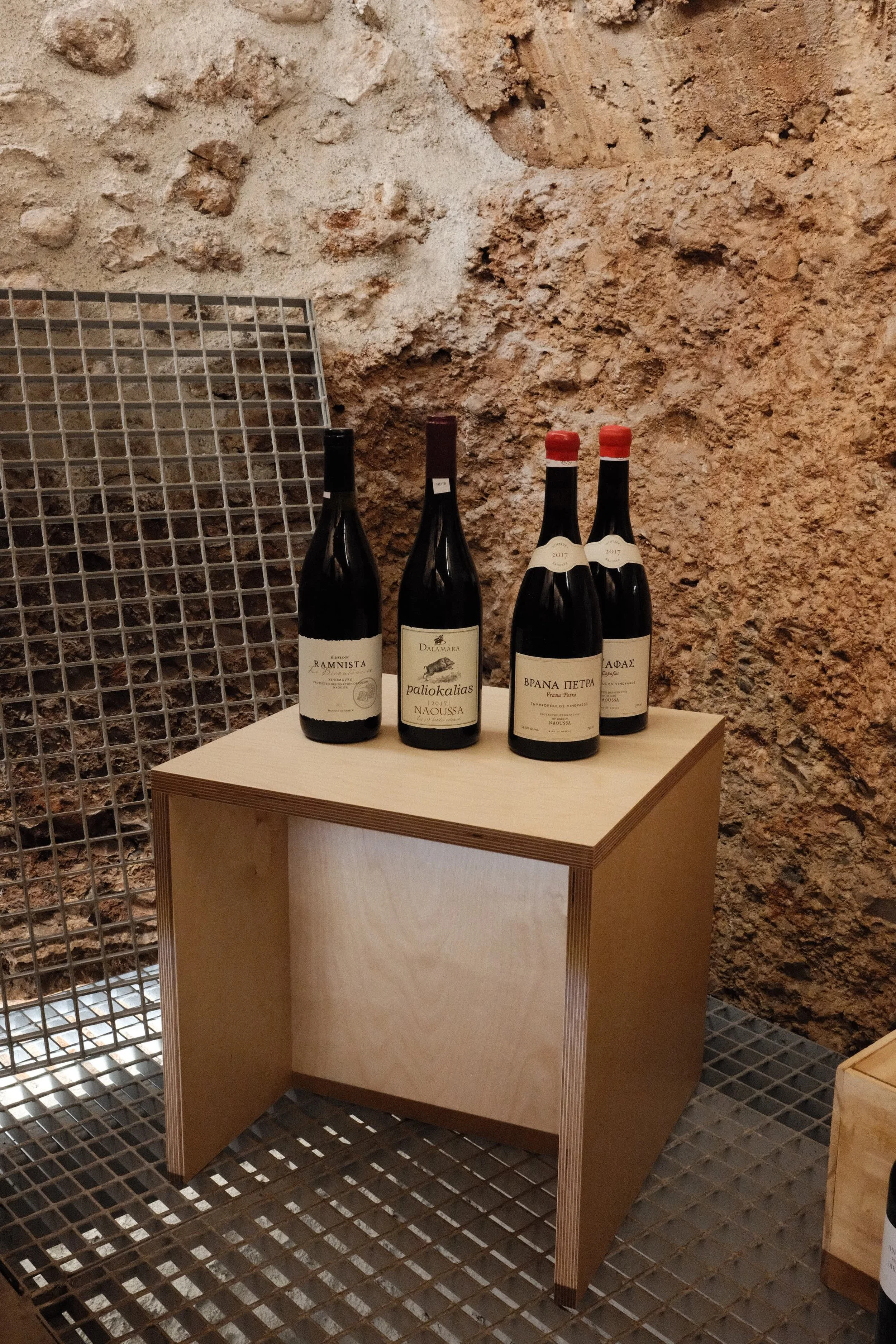 Four bottles of wine displayed on a wooden table against a textured stone wall.