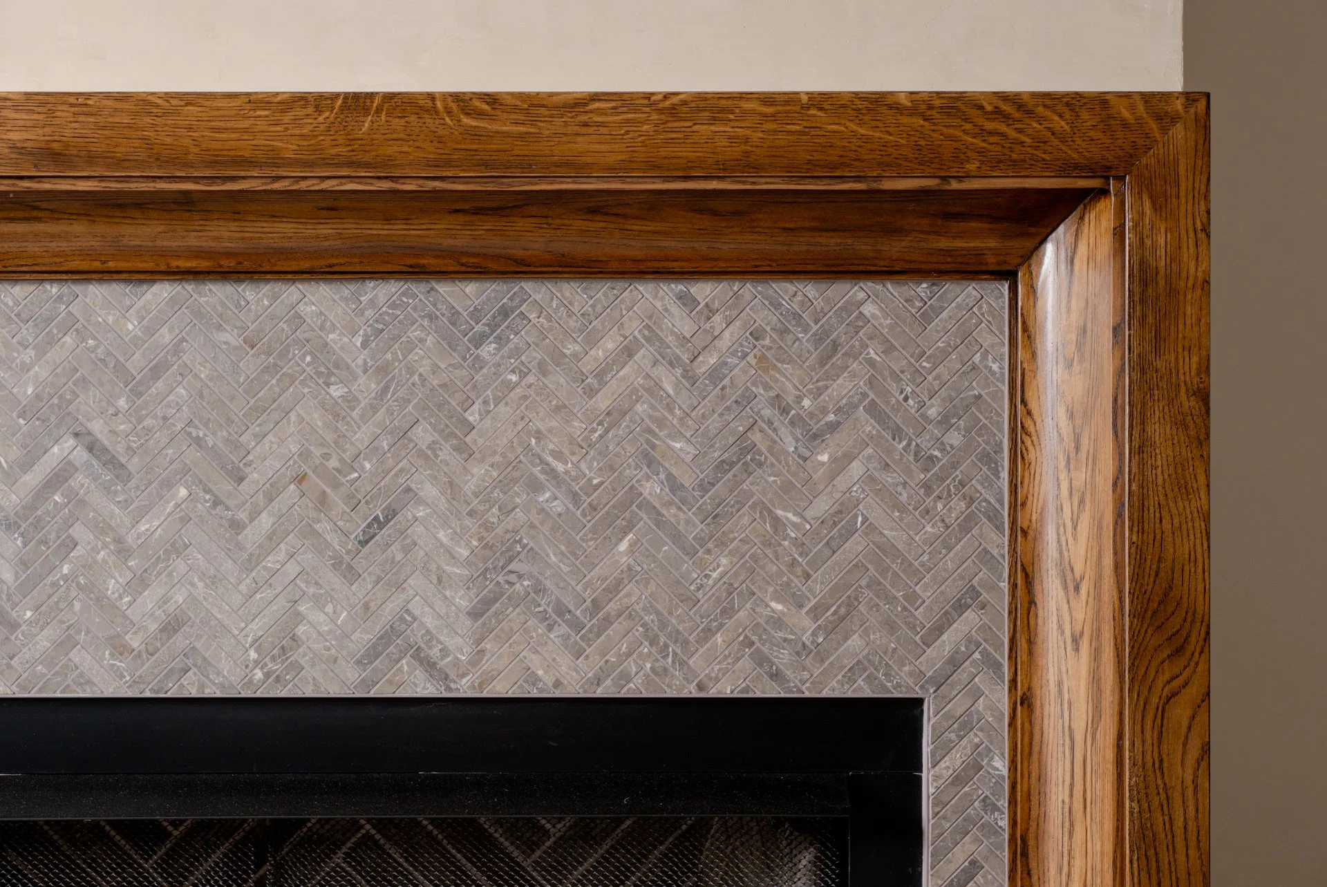 A stunning fireplace with a small herringbone grey tile and a warm wood mantle.