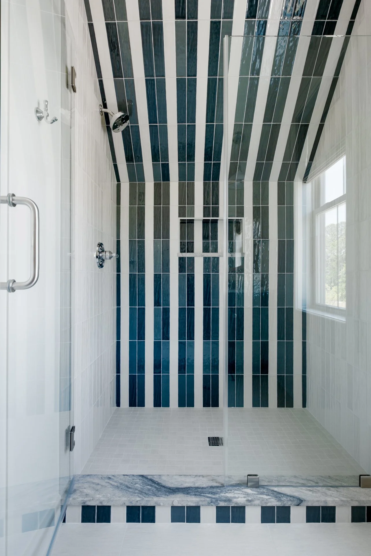 A custom-cut guest shower with a slanted ceiling, striped blue and white tile pattern, and a slab curb.