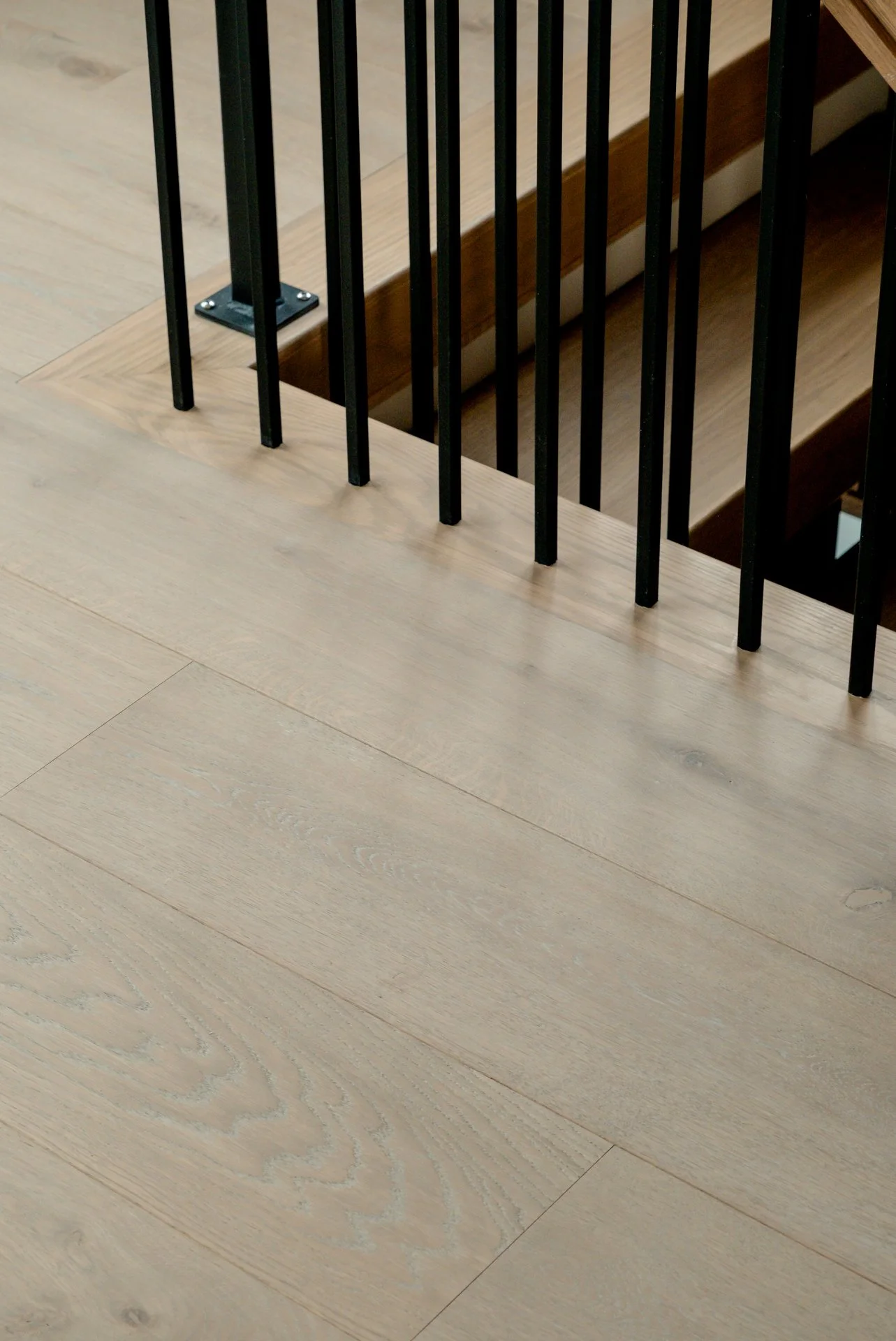 Close-up of a wooden staircase and floor with black metal railing.