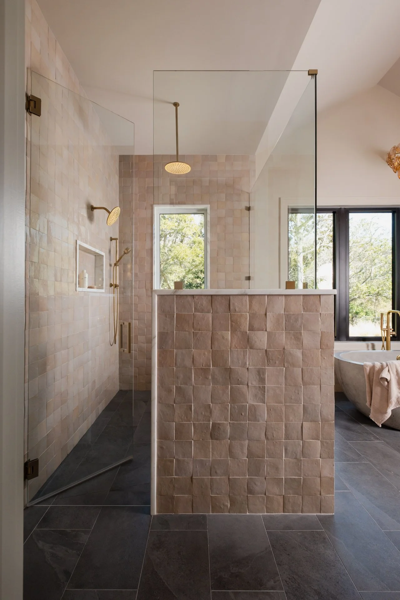 A large master bathroom shower with an overhead rain shower faucet, a fixed wall shower head, and a large custom niche. Wrapped in Tiles of Ezra Zellige 4x4 oat colored tiles with a Wayne Tile Ultra Slate Dark Gray 12x24 floor tile.