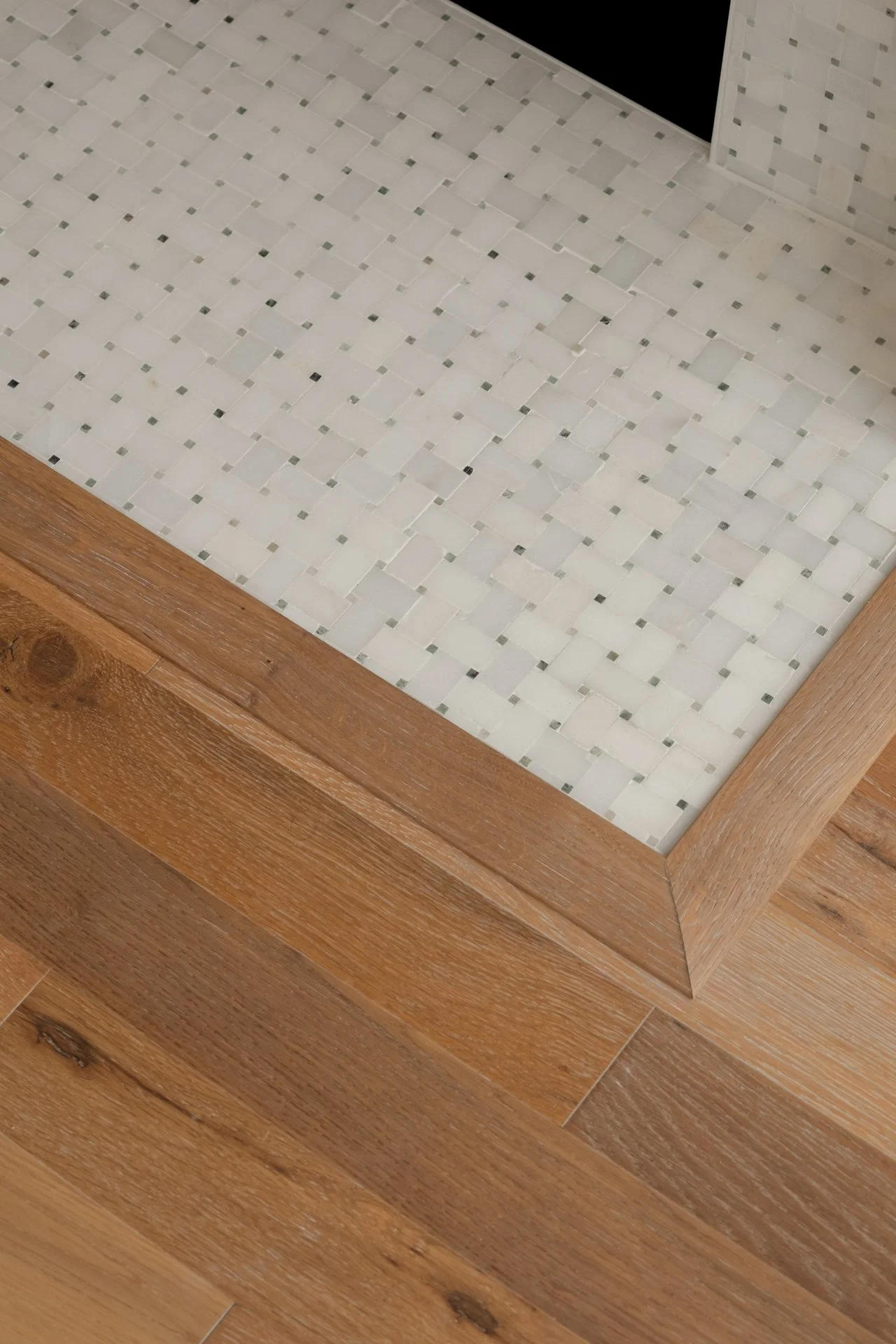 Close-up of a corner with white mosaic tiles and a wooden floor.