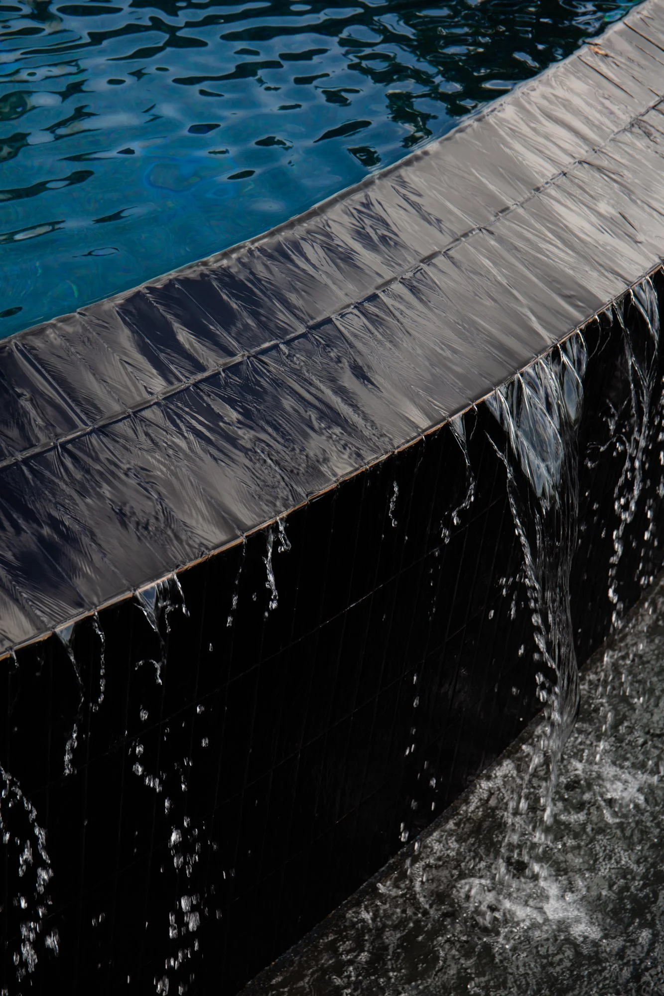 Close-up of a modern black stone water feature with water cascading over the edge into a pool below.