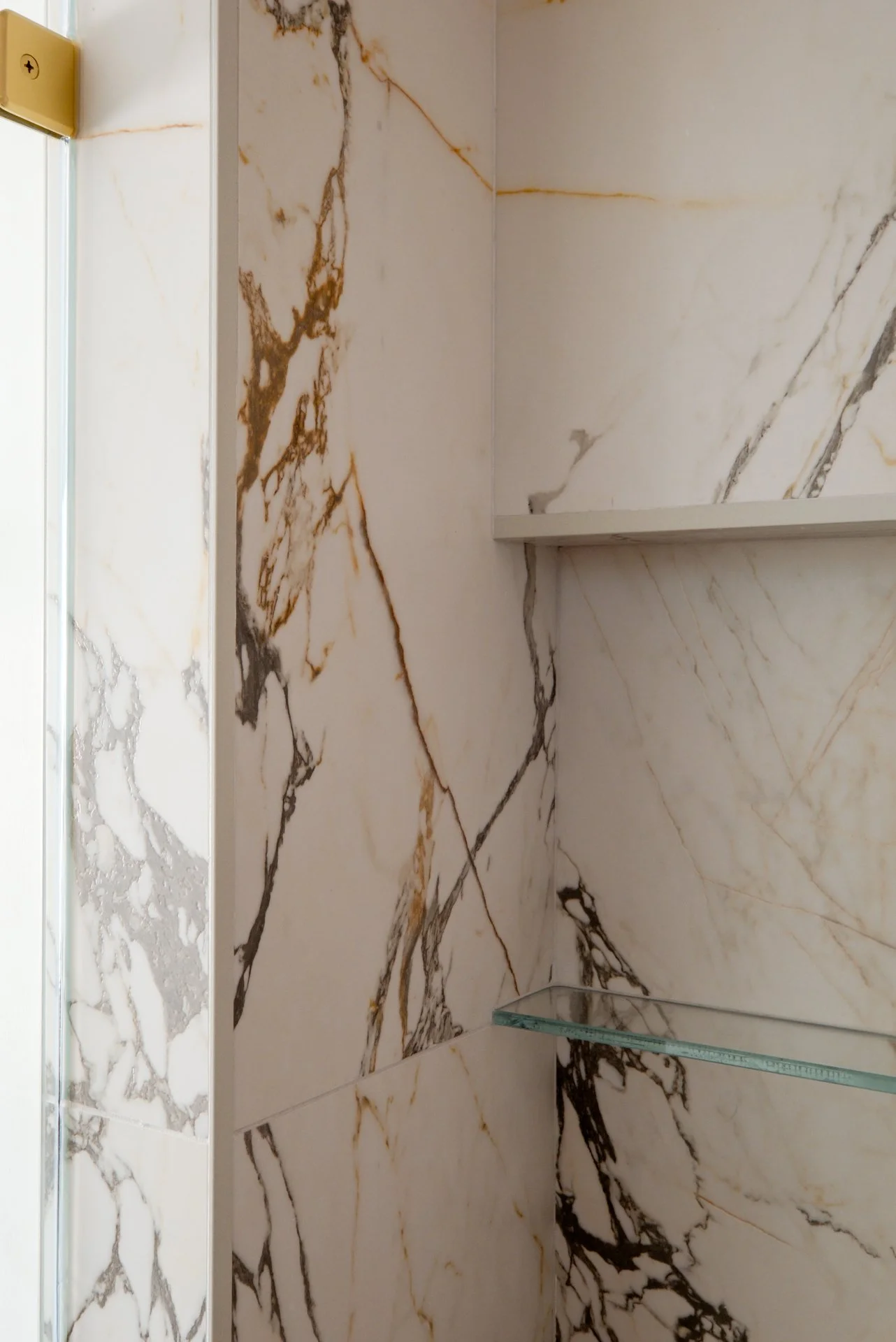 A large format master shower with Nemo Tile Leon Arabescato in 24x48 — Bold veining, timeless movement, and a scale that makes the entire space feel elevated and intentional seamlessly flowing into the custom niche.  Gold shower fixtures to pull out 