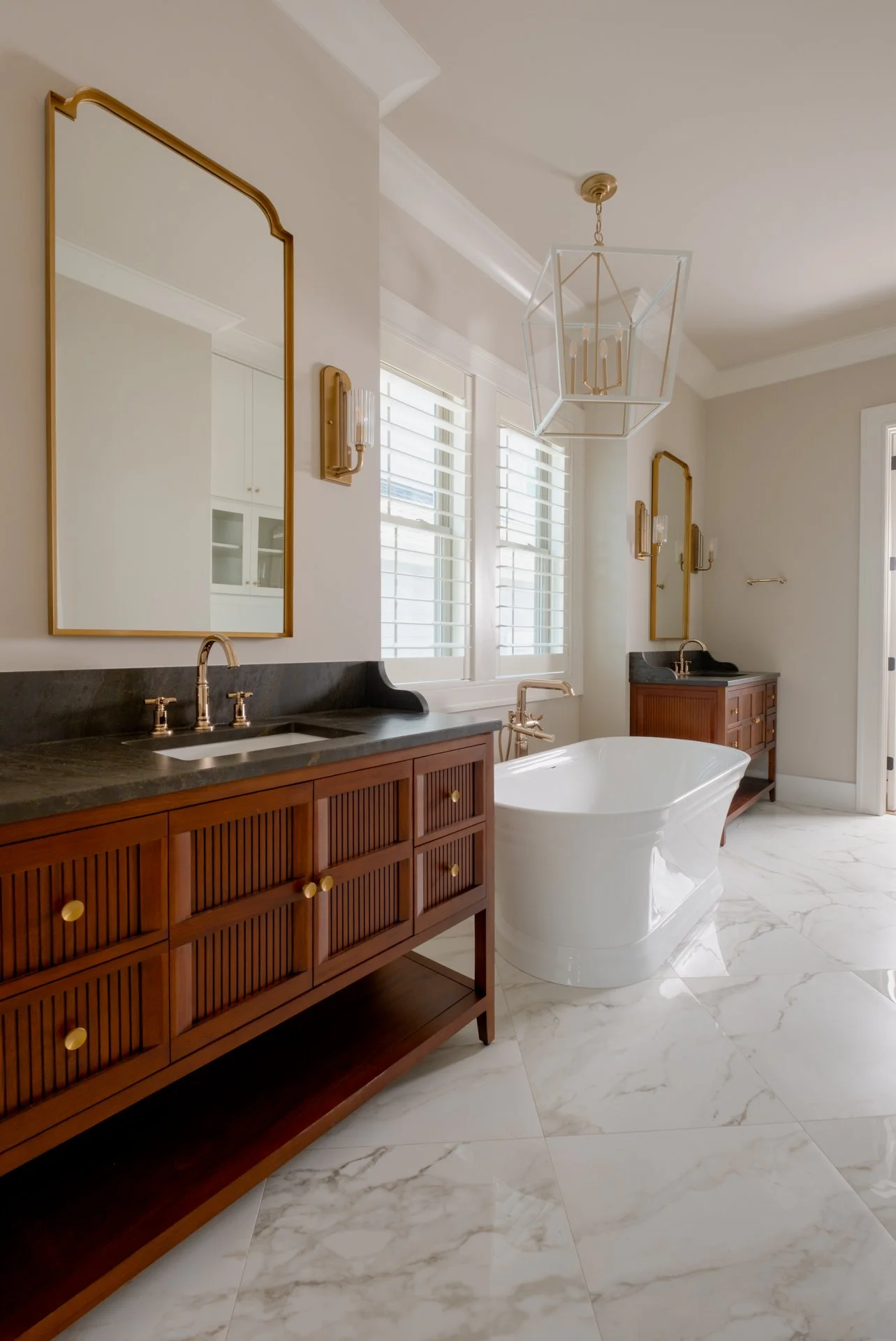 A luxury master bath with custom cabinets, black countertops, a freestanding bath tub and large checkerboard pattern tiled floors.