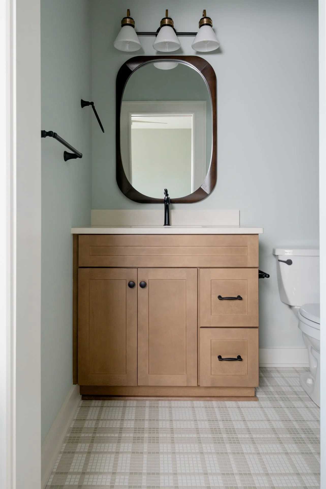 A guest bath with plaid tile floors and oak wood cabinets with black finishes.