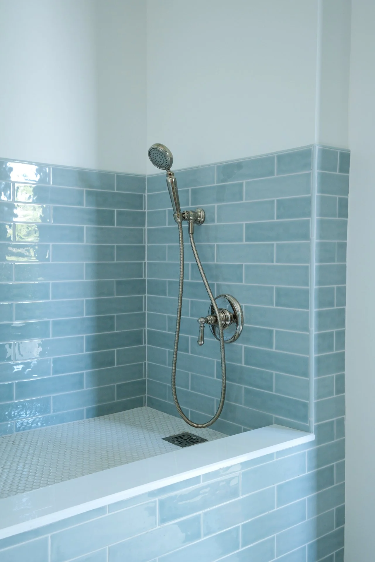 Shower area with blue subway tiles, a handheld showerhead, and a drain on the shower floor.