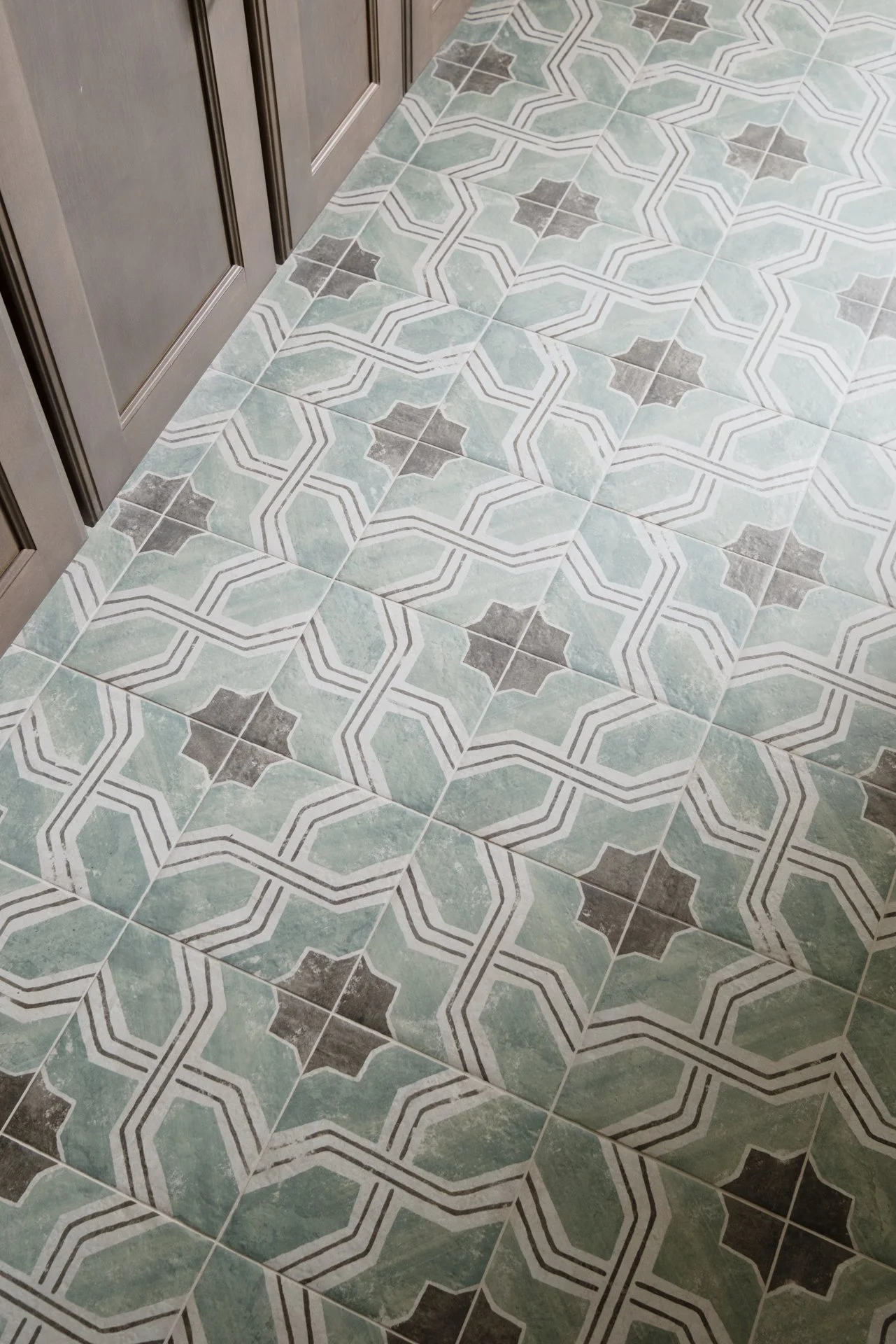 A close-up of a laundry room floor with patterned tile in greens and browns, tying in the brown custom cabinetry.