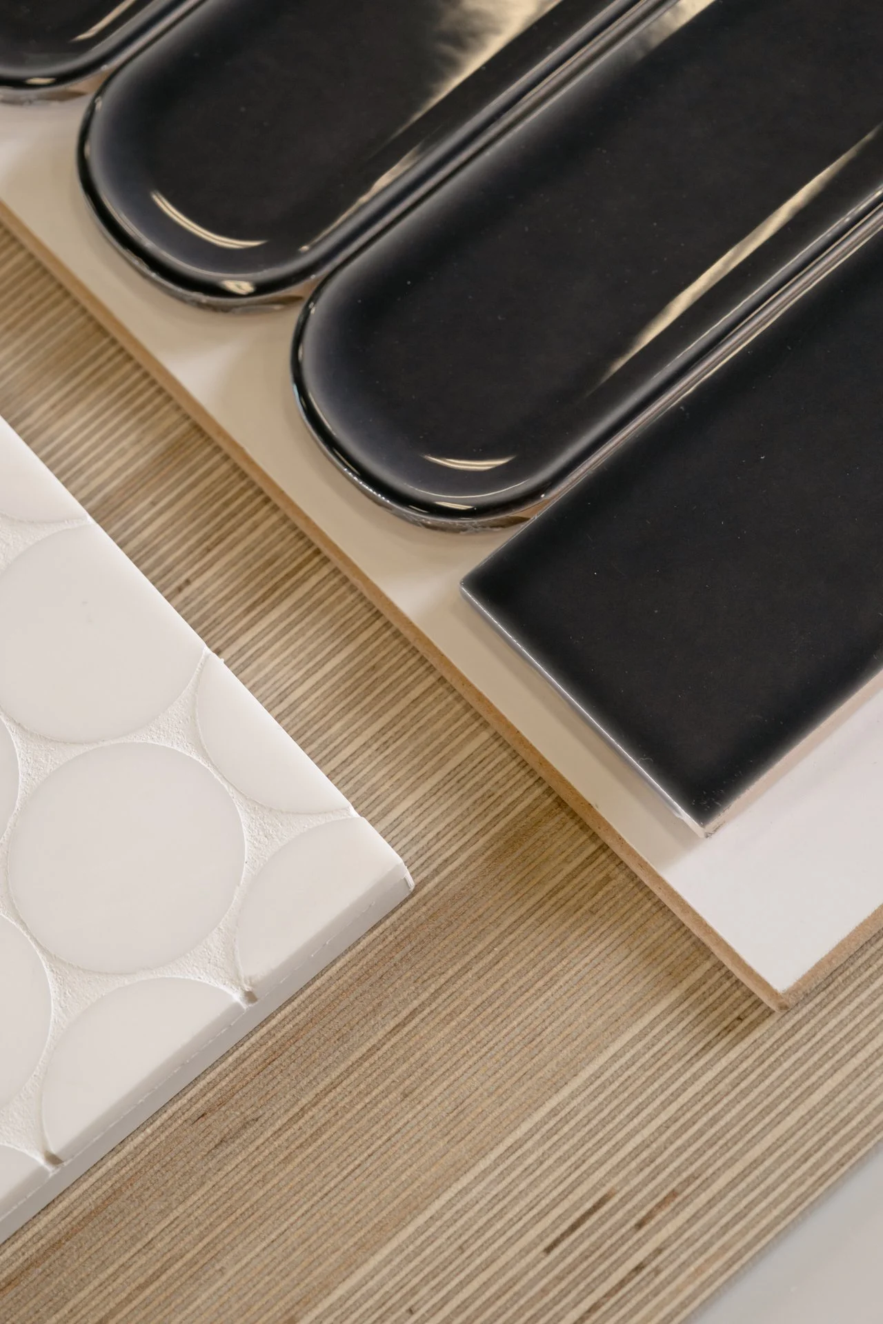 Tile samples at the Refine Tile and Design showroom in Wilmington, NC. Close-up of black ceramic tiles on a white surface and a textured surface with a white panel featuring circular indentations.