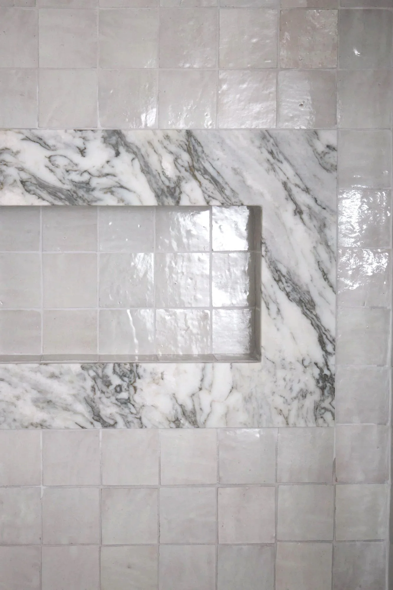 Top view of a marble shower niche with gray and white veining, surrounded by beige square tiles with a glossy finish.