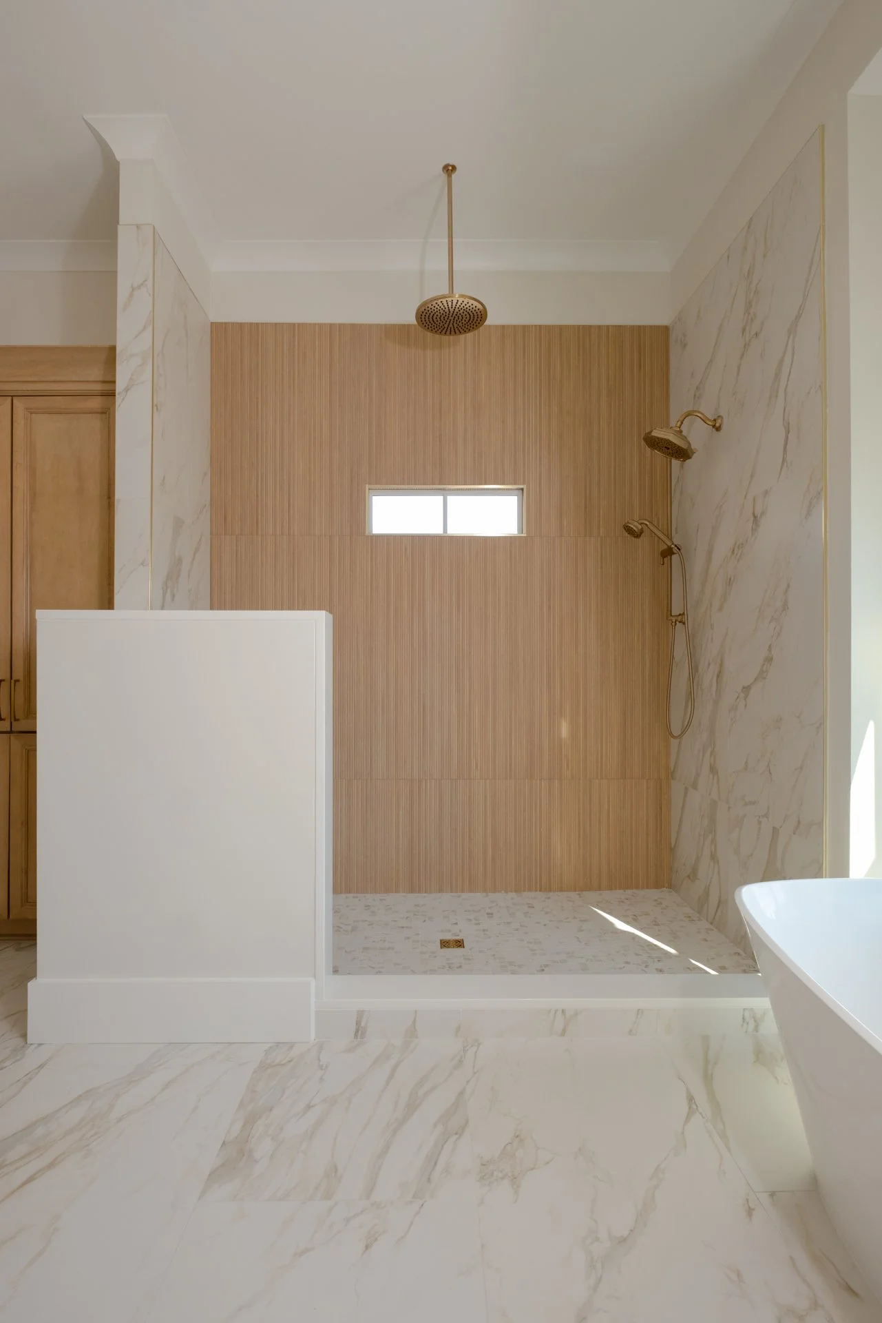 A master walk-in shower with Calcatta all throughout, large format and mosaic, with a focal wall from Best Tile in Ice Nebraska Tea. Intentionally layered space.