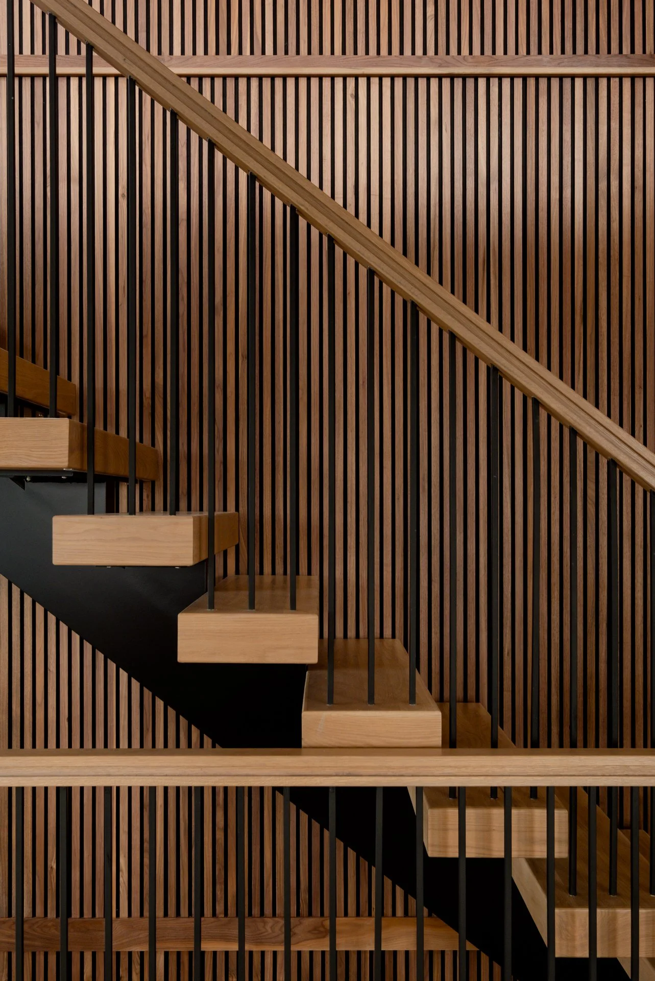 Wooden staircase against a wall with vertical wood slats and black support beams.