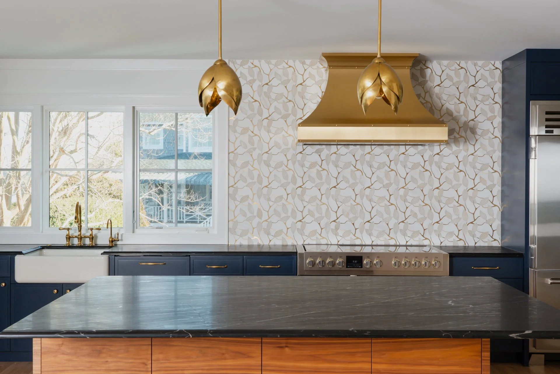 A custom backsplash created with Mosaique Surface incorporating metallic materials with a subtle floral design. Ties in perfectly with the metallic gold range hood, finishes, and dark two-toned cabinetry with black tops.
