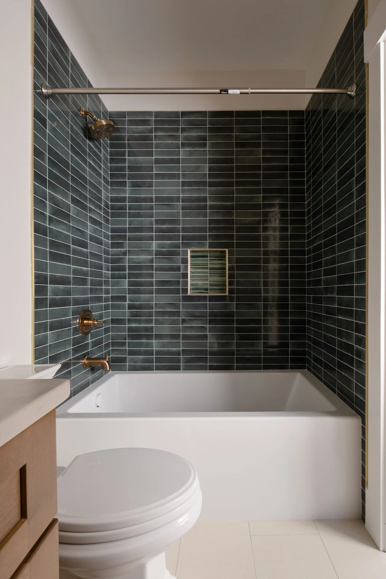A full shot of a guest bathroom shower with blue color variation tile, in a horizontal subway stack with gold finishes. 