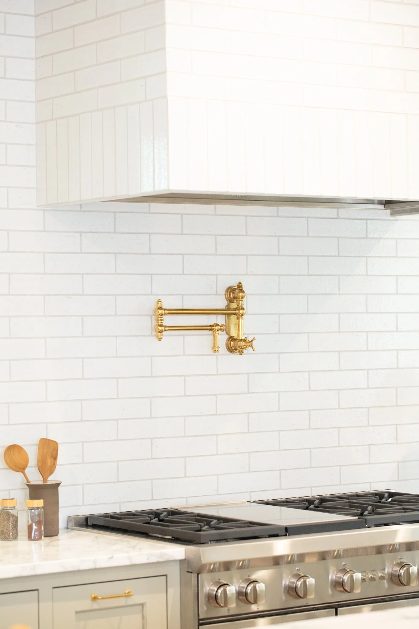 Modern kitchen with white brick backsplash, stainless steel gas stove, and brass pot filler faucet above the stove.