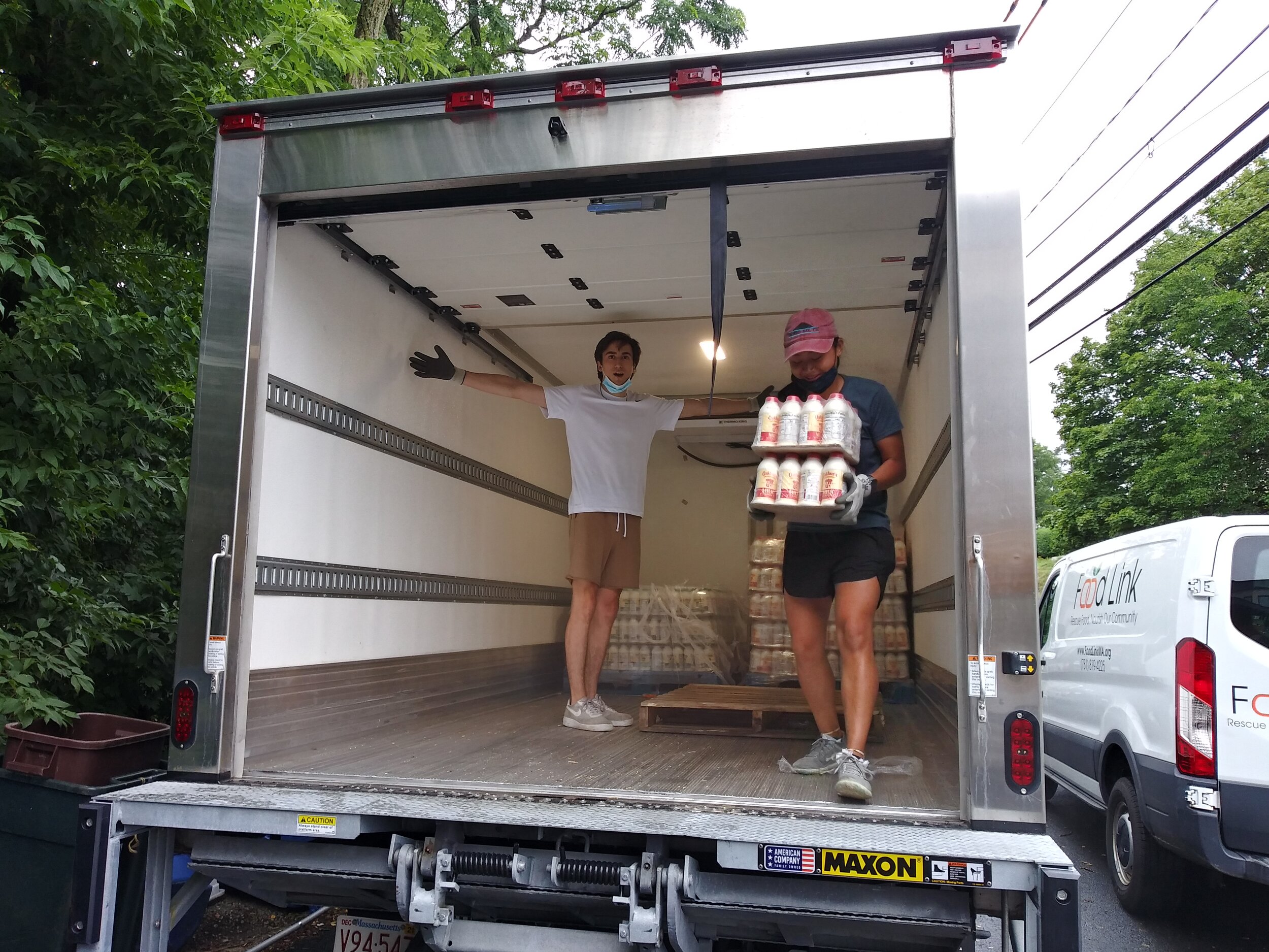 Two Food Link volunteers stand in a truck holding cartons of milk