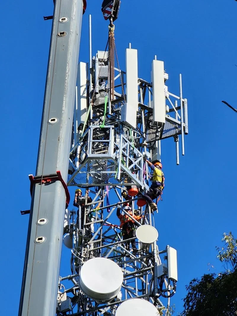 Technicians working on a telecommunications tower against a clear blue sky.