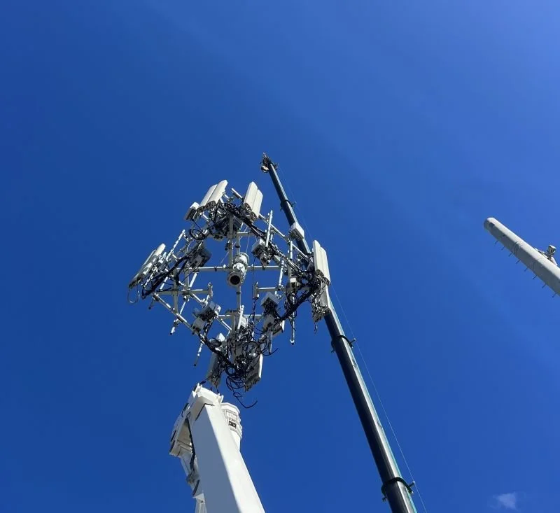 Cell tower with multiple antennas and equipment against a clear blue sky.