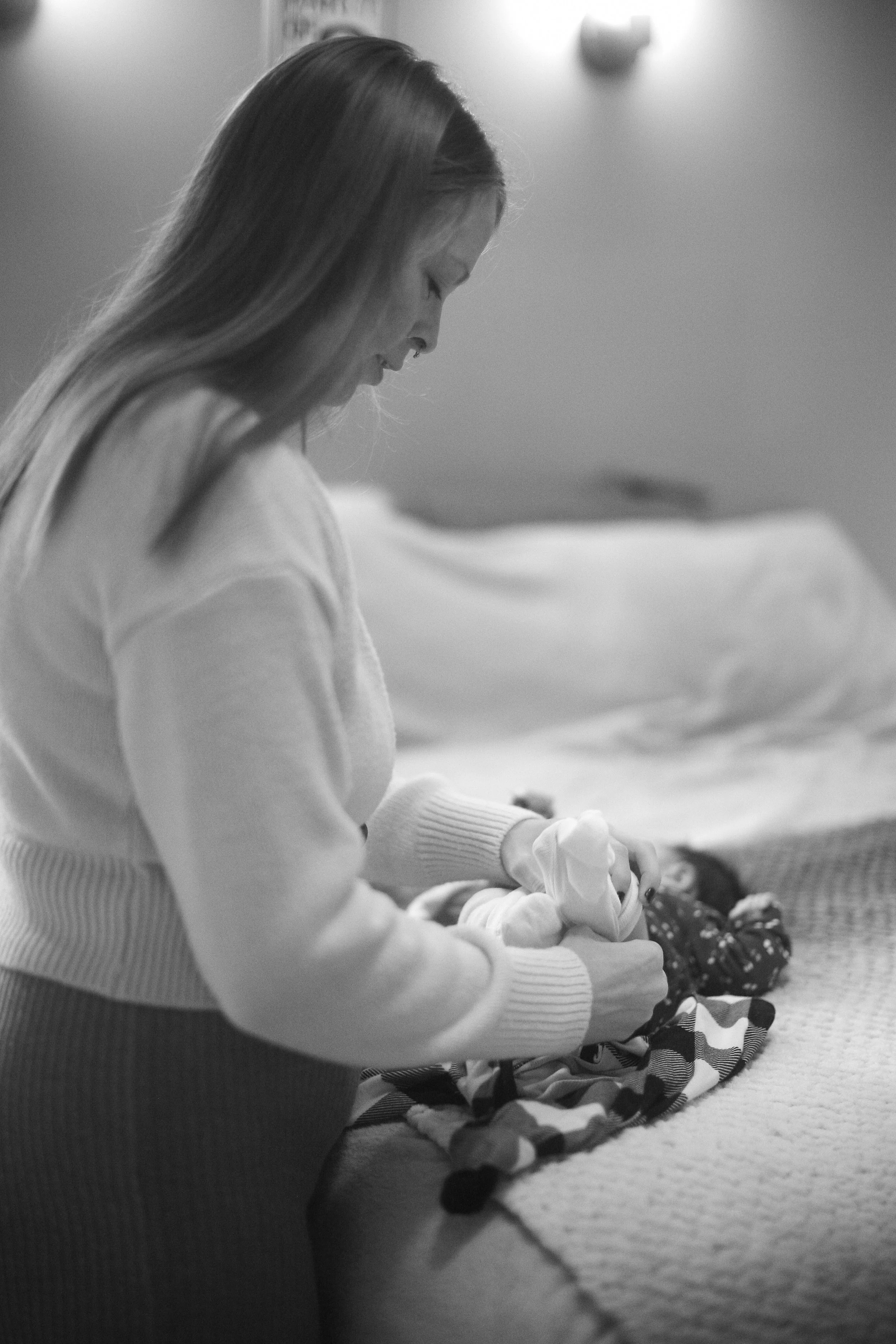 Woman wrapping a baby in a blanket on a bed in a softly lit room.