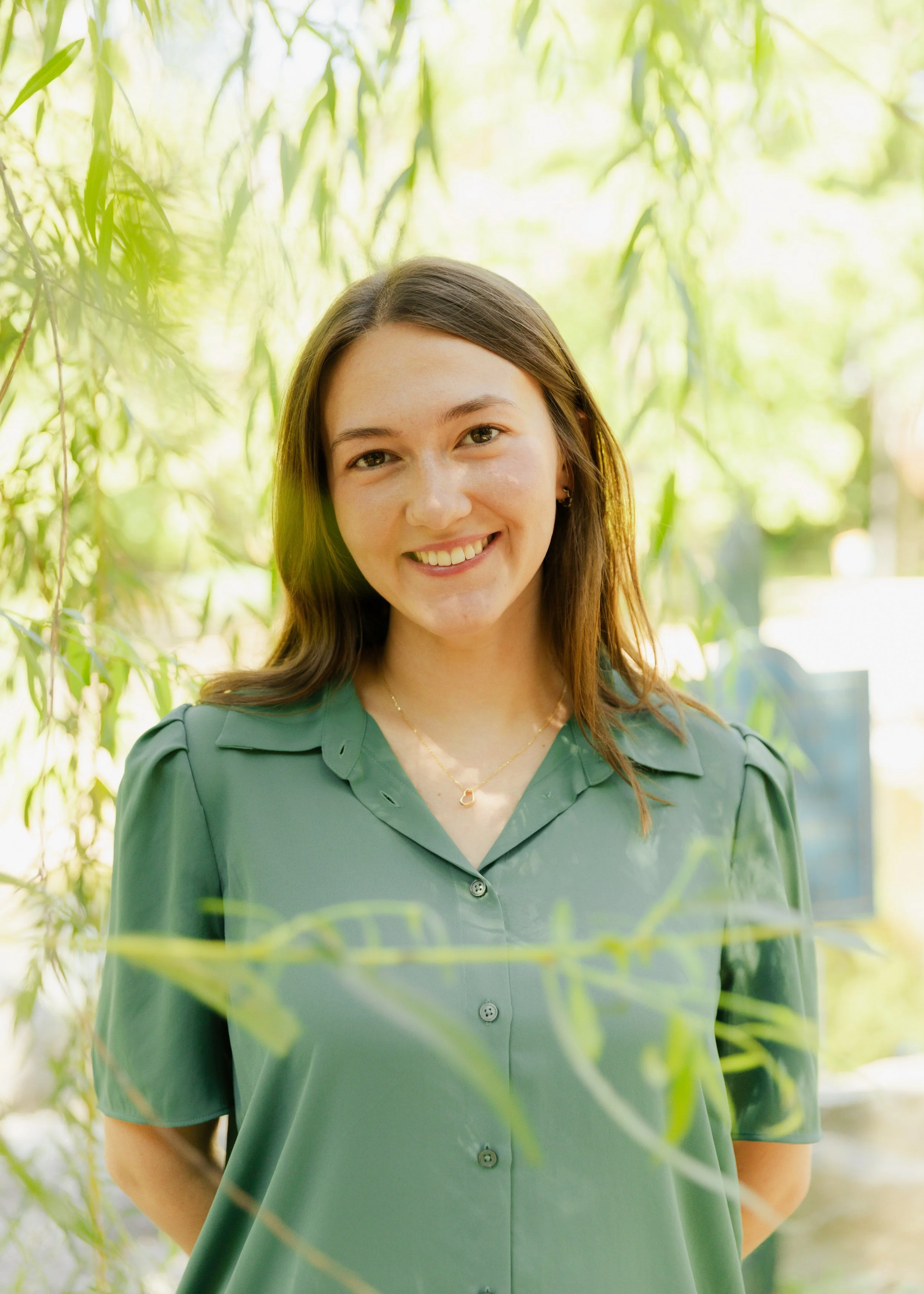Headshot of woman standing with tree details in foreground and background