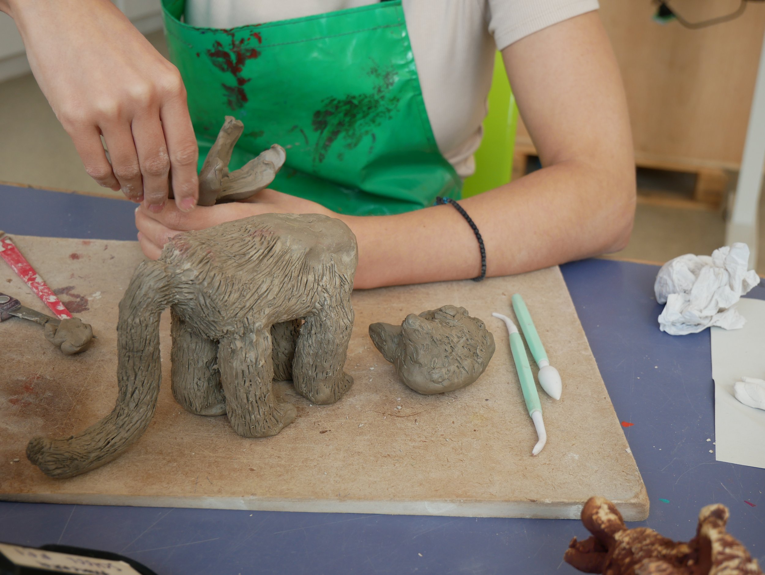  Leslie and Eleni working on clay animal sculptures together in the Venture Arts studio. Leslie is on the left and Eleni is on the right, both working on wooden boards. The photos show the animals in varying places along the journey of becoming full 