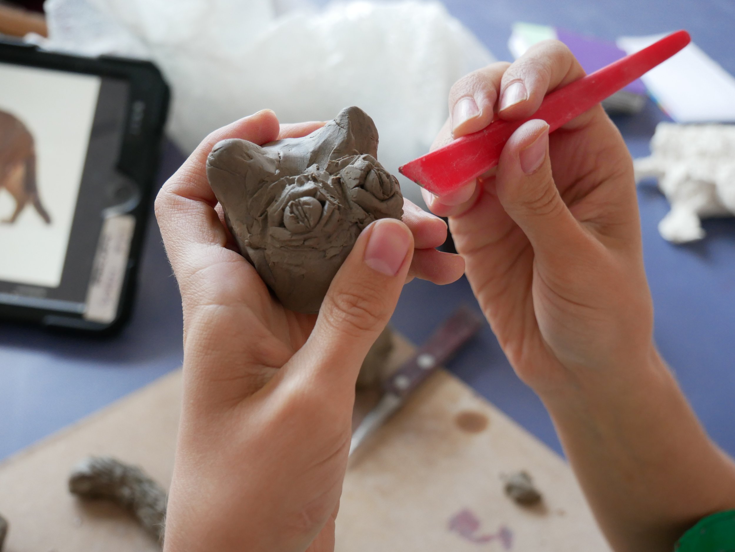  Leslie and Eleni working on clay animal sculptures together in the Venture Arts studio. Leslie is on the left and Eleni is on the right, both working on wooden boards. The photos show the animals in varying places along the journey of becoming full 