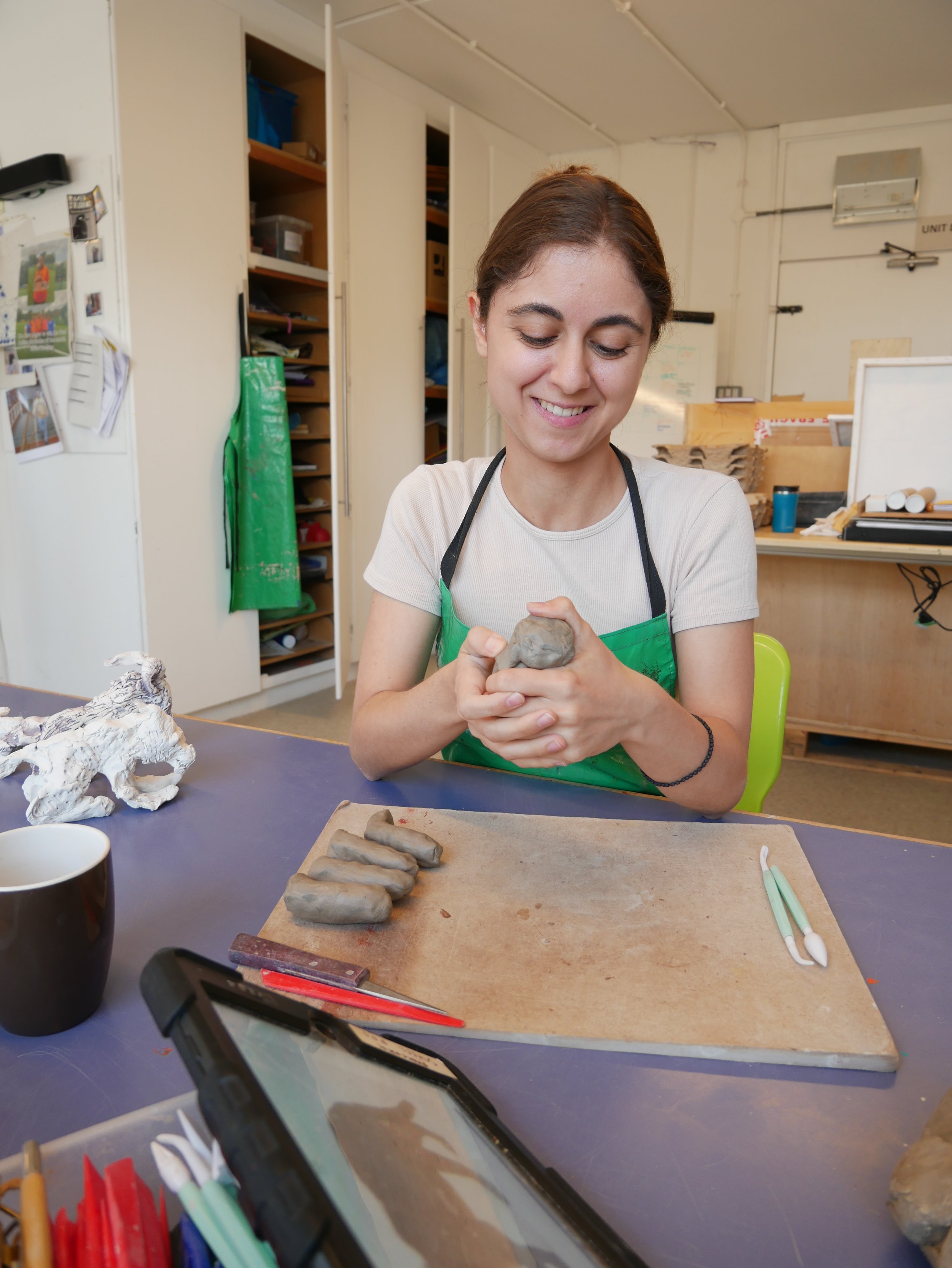  Leslie and Eleni working on clay animal sculptures together in the Venture Arts studio. Leslie is on the left and Eleni is on the right, both working on wooden boards. The photos show the animals in varying places along the journey of becoming full 