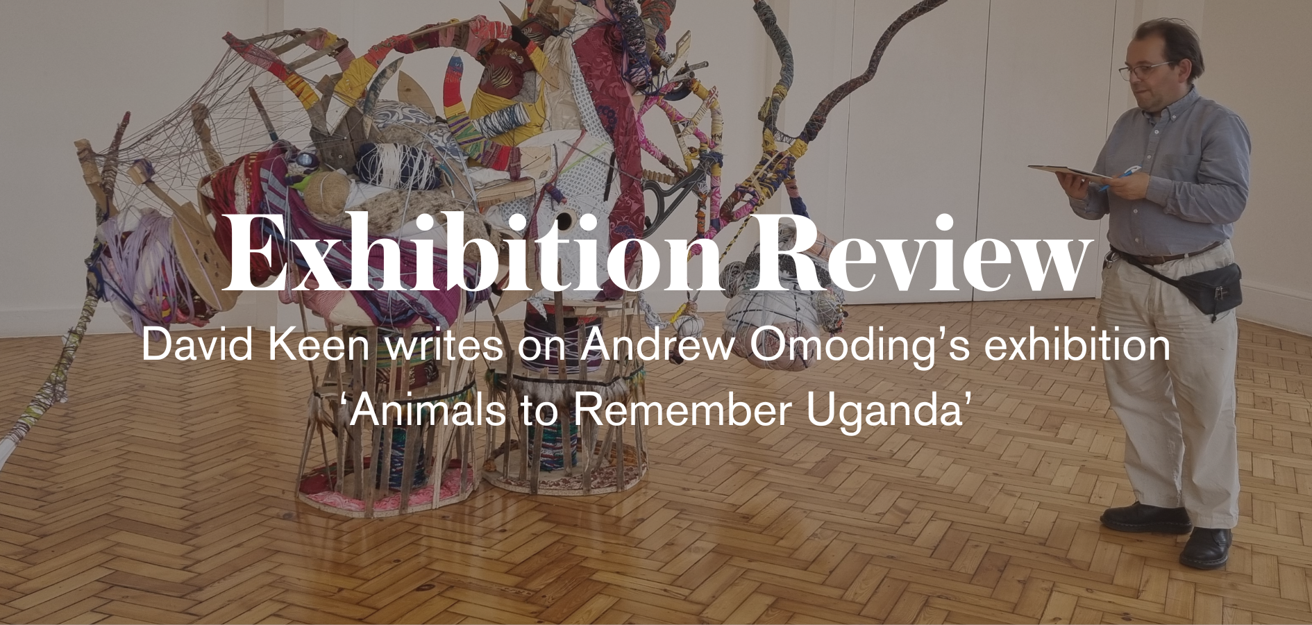an image of a brightly coloured sculpture featuring wood wrapped in textile. And a person with a blue shirt and cream trousers standing to the right of the photo next to the sculpture. In white the text reads 'exhibition review. David Keen writes'