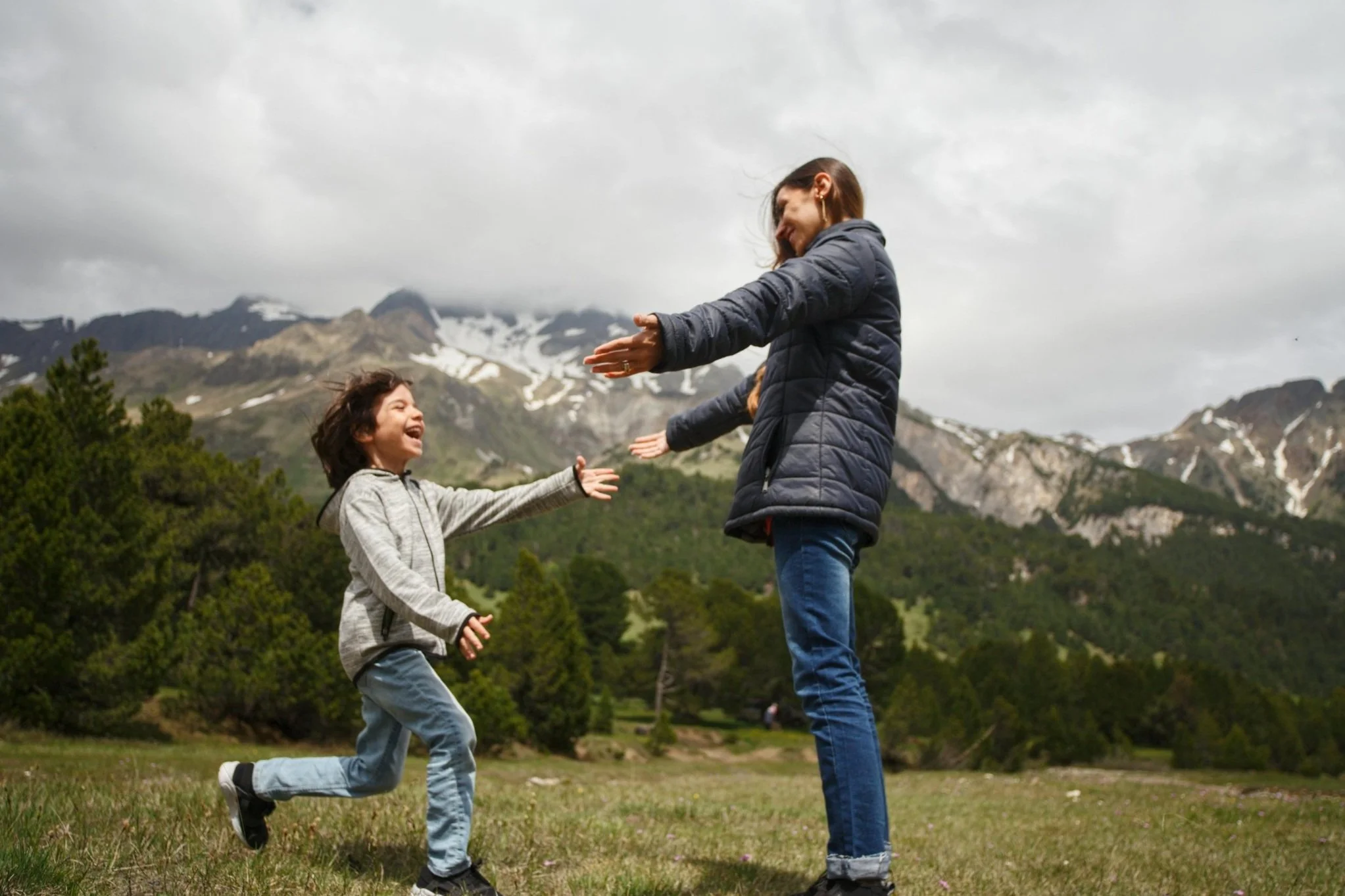 Mother and daughter outdoors in mountain landscape, smiling and reaching out to each other.