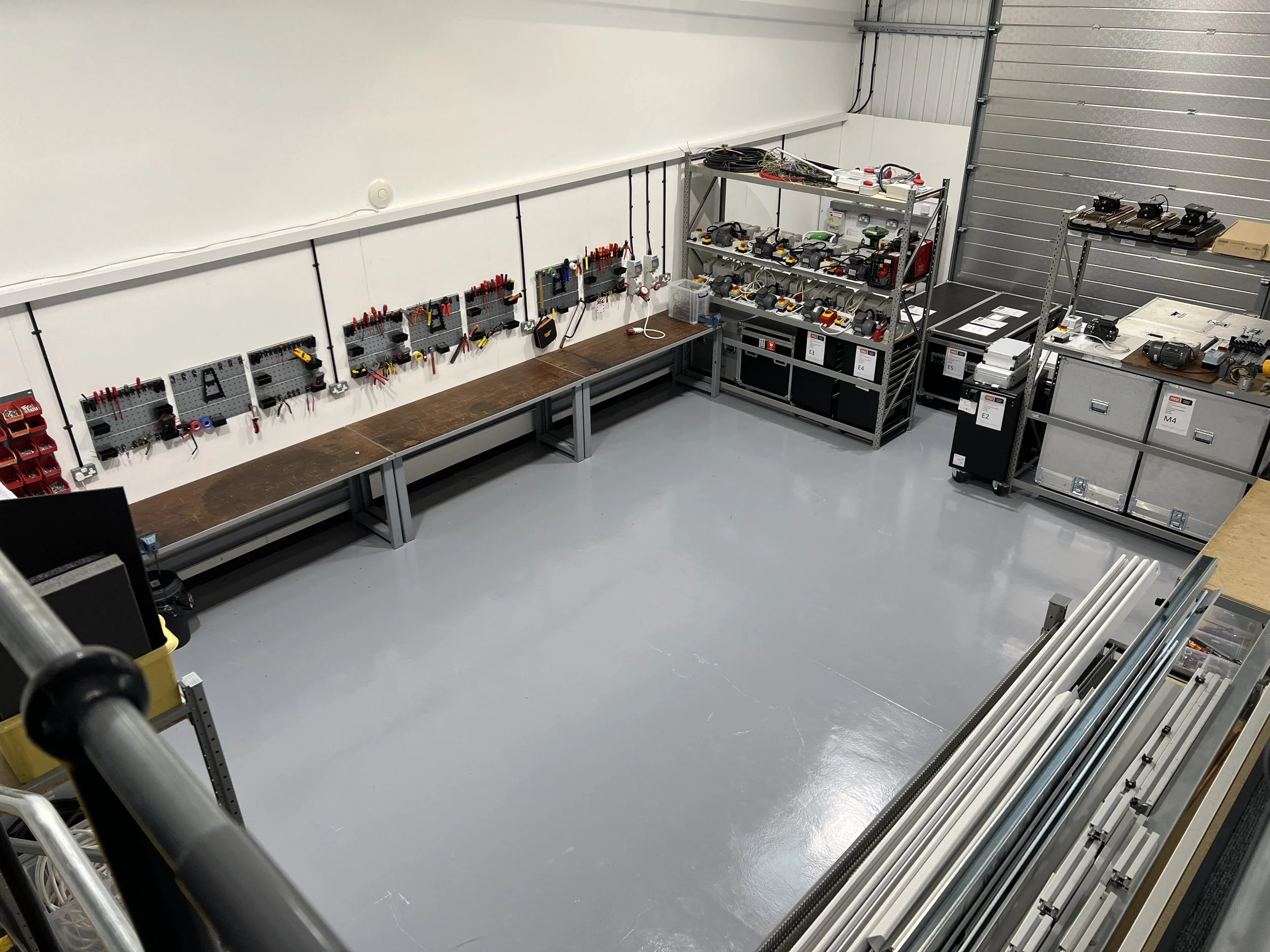Workshop with organized tools, equipment, and storage shelves, with a long workbench along the wall and metal racks filled with power tools and supplies.