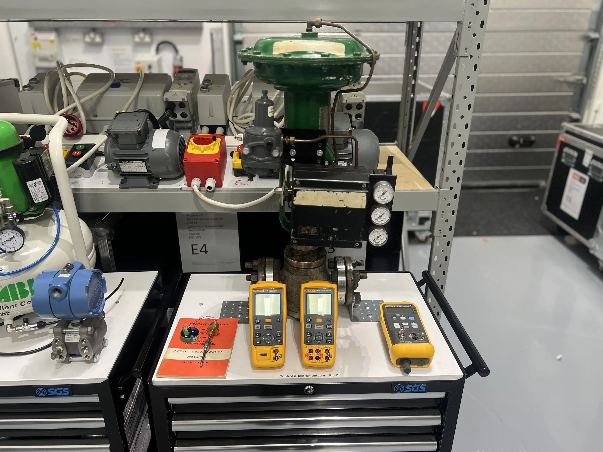 Test setup with a valve, gauges, and electronic testing devices on a white workbench in an industrial lab.