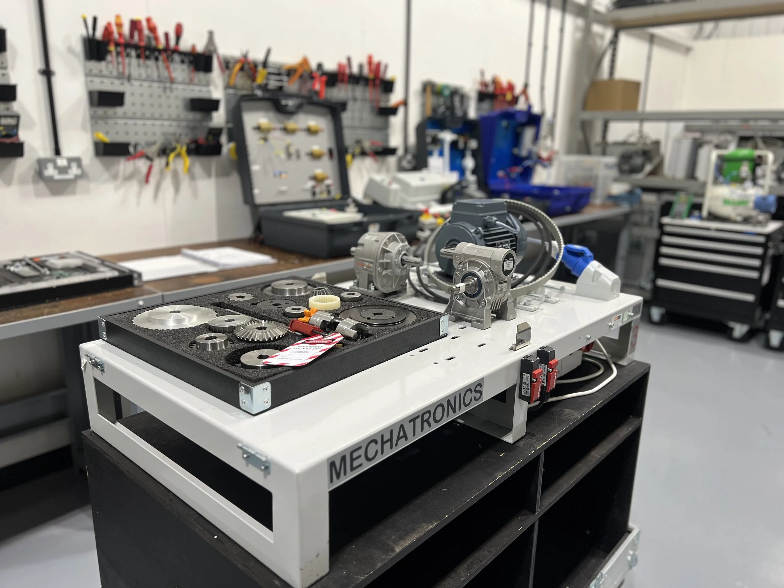 Workstation with mechanical parts and gears, in a workshop with tools and equipment in the background.