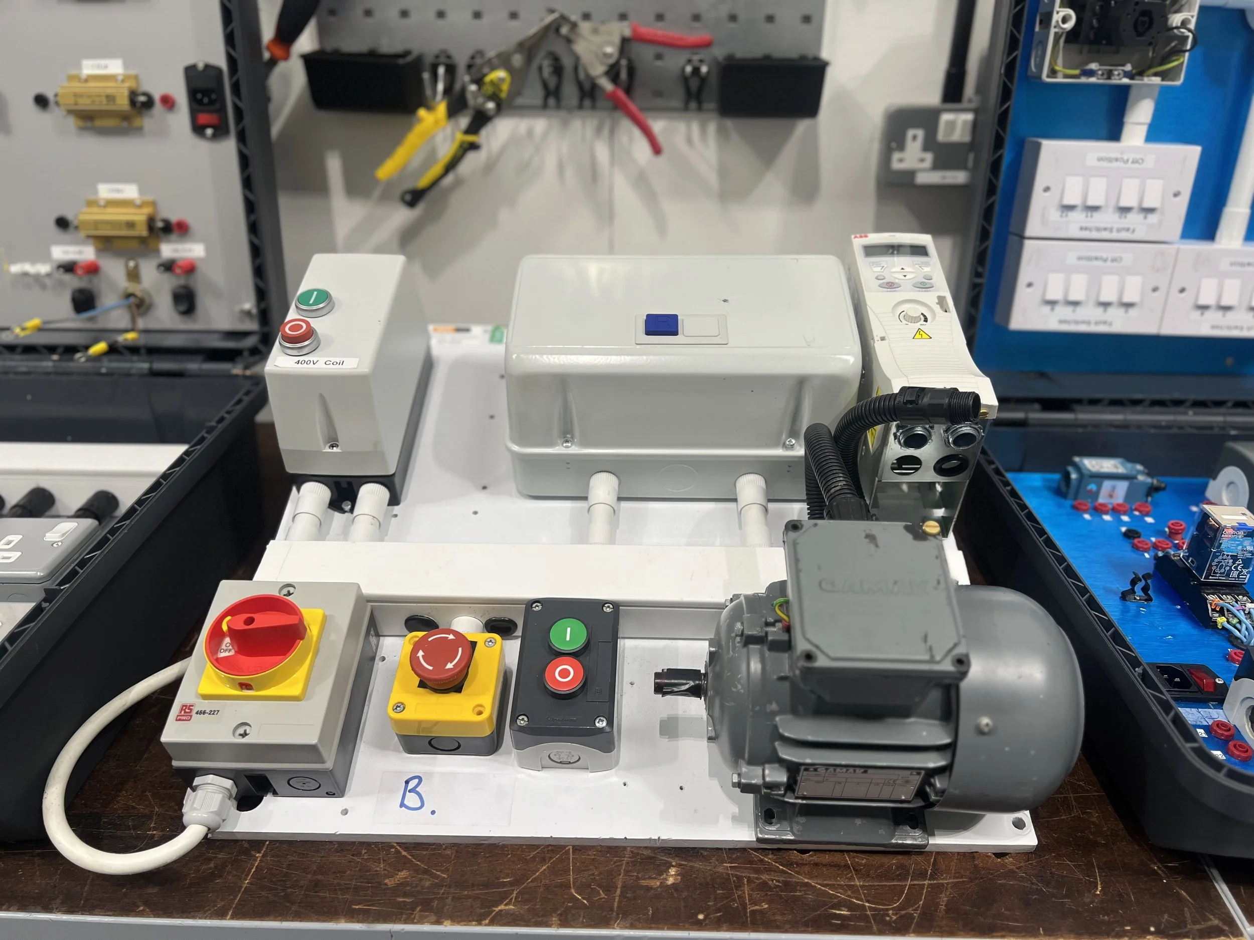 Electrical training setup with control panel, motor, switches, and wiring on a table.