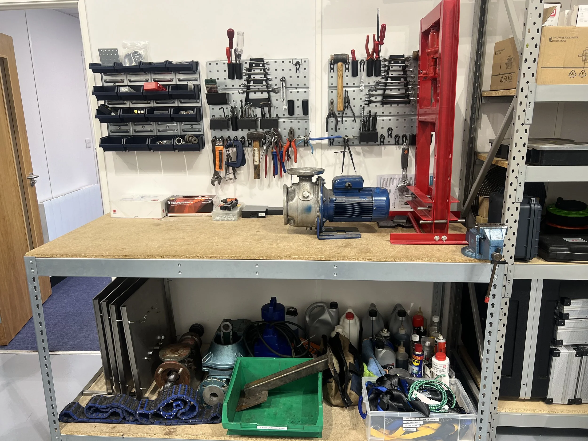 Organized workshop workspace with tools on pegboard, motor, red metal frame, and various supplies on shelves and workbench.