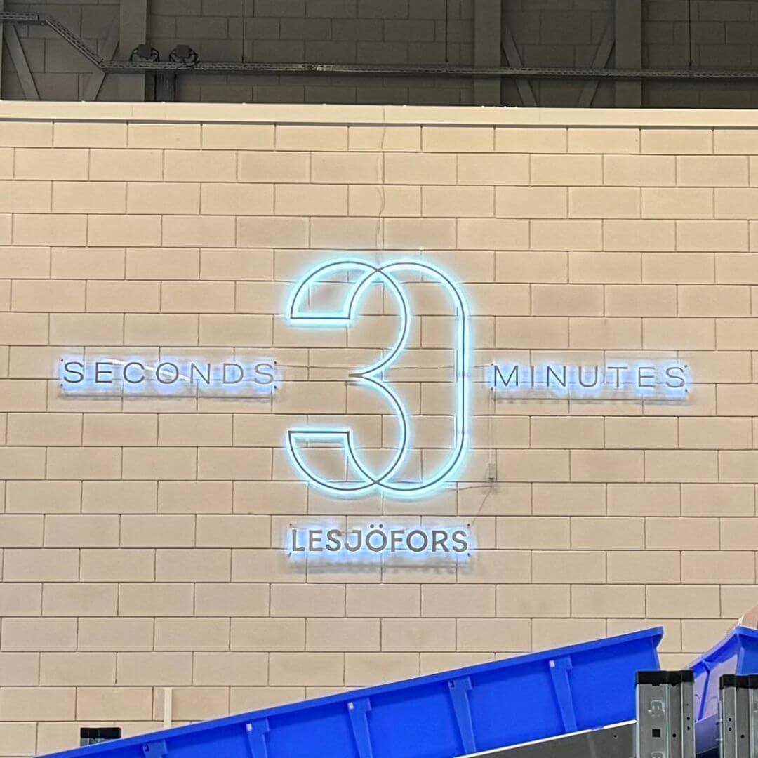 Neonskylt med ”30 seconds / 30 minutes” på väggen i Lesjöfors centrallager, symbol för företagets e-handelsinspirerade plock- och leveranslöfte. 