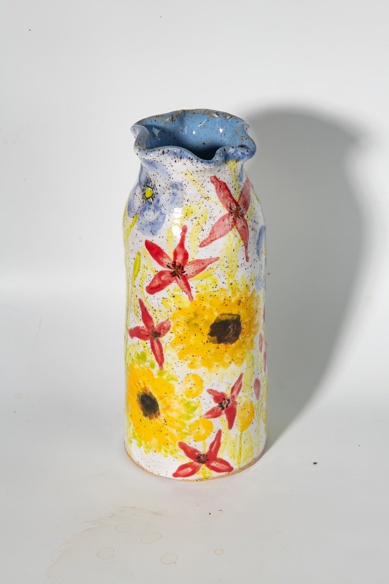 2nd view of tall ceramic scalloped vase covered in hand painted sunflowers, cardinal flowers and poppies