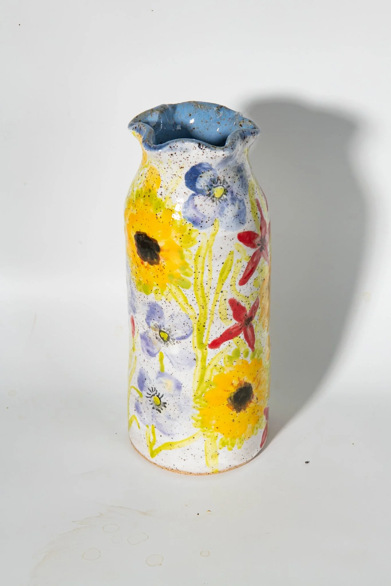 View of tall scalloped ceramic vase hand painted with sunflowers, cardinal flowers and poppies