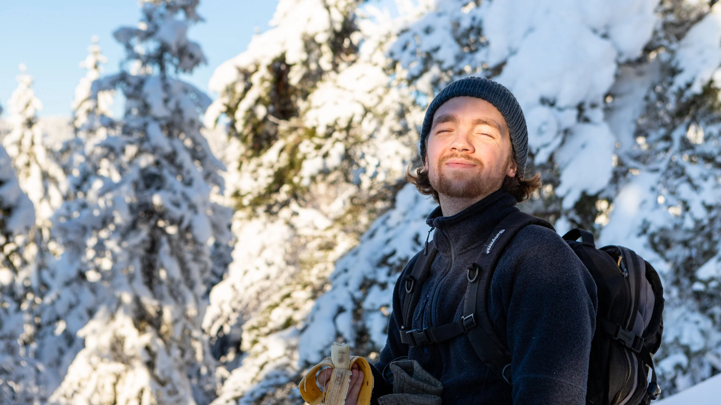 Smilende mann spiser banan i sola i snøen